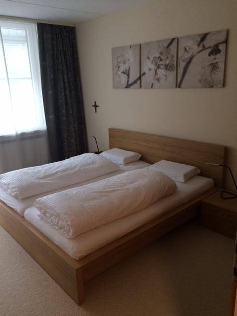 Schlafzimmer mit hellem Holzbett, Nachttischen und Fenster mit Jalousien für erholsamen Schlaf.