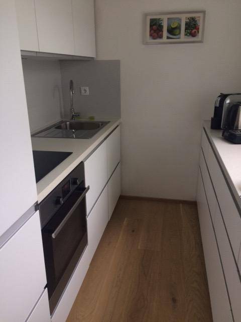 Schmale, moderne Küche mit weißen Schränken, integriertem Backofen und Holzboden für effizientes Kochen.