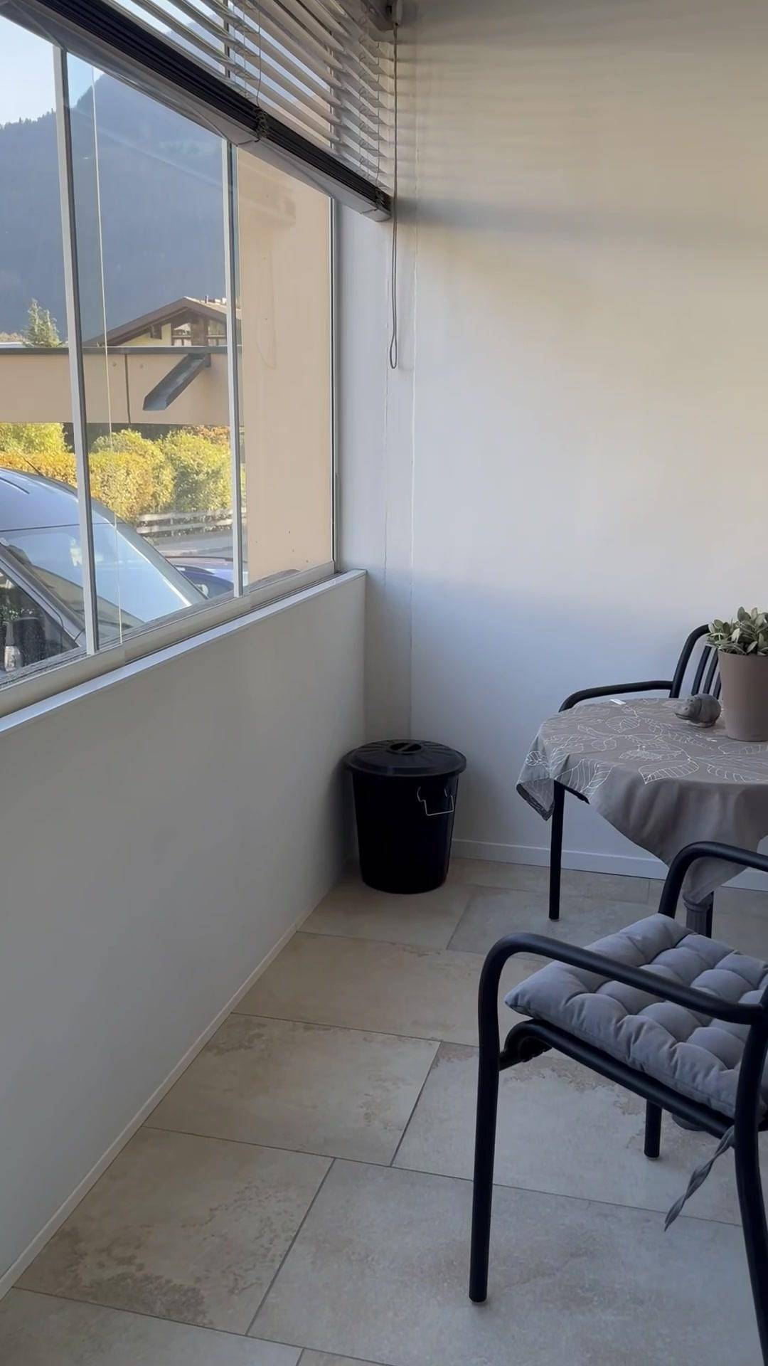 Verglaster Balkon mit Fliesenboden, Sitzgelegenheiten und Blick auf die Berge.