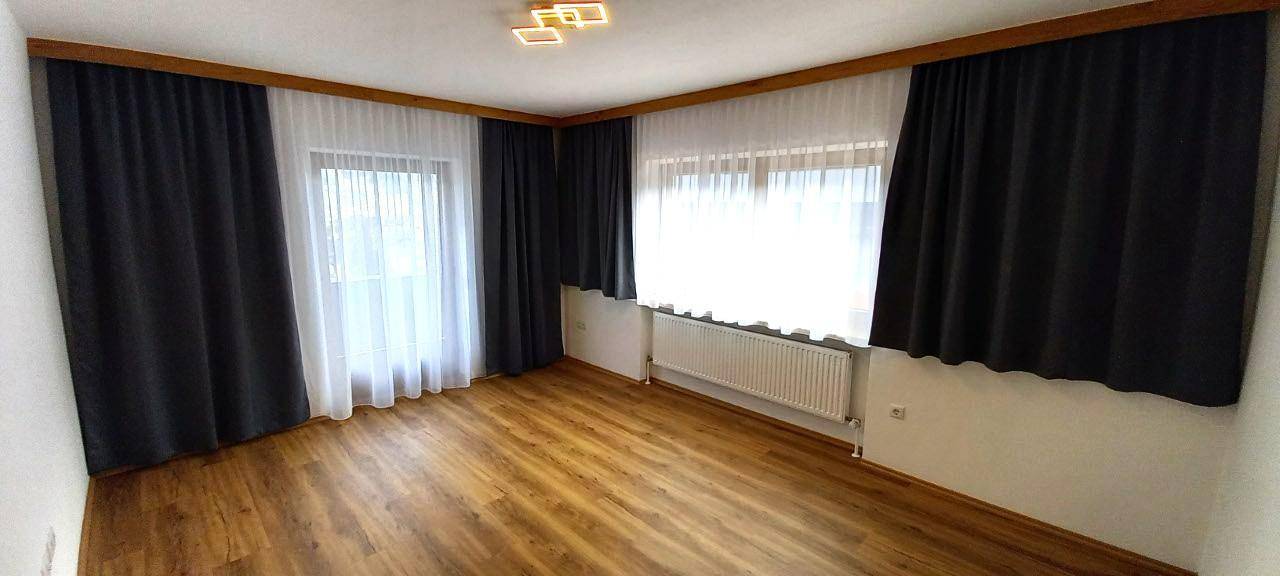 Helles Schlafzimmer mit Holzboden, großzügigen Fenstern und dunklen Vorhängen für Privatsphäre.