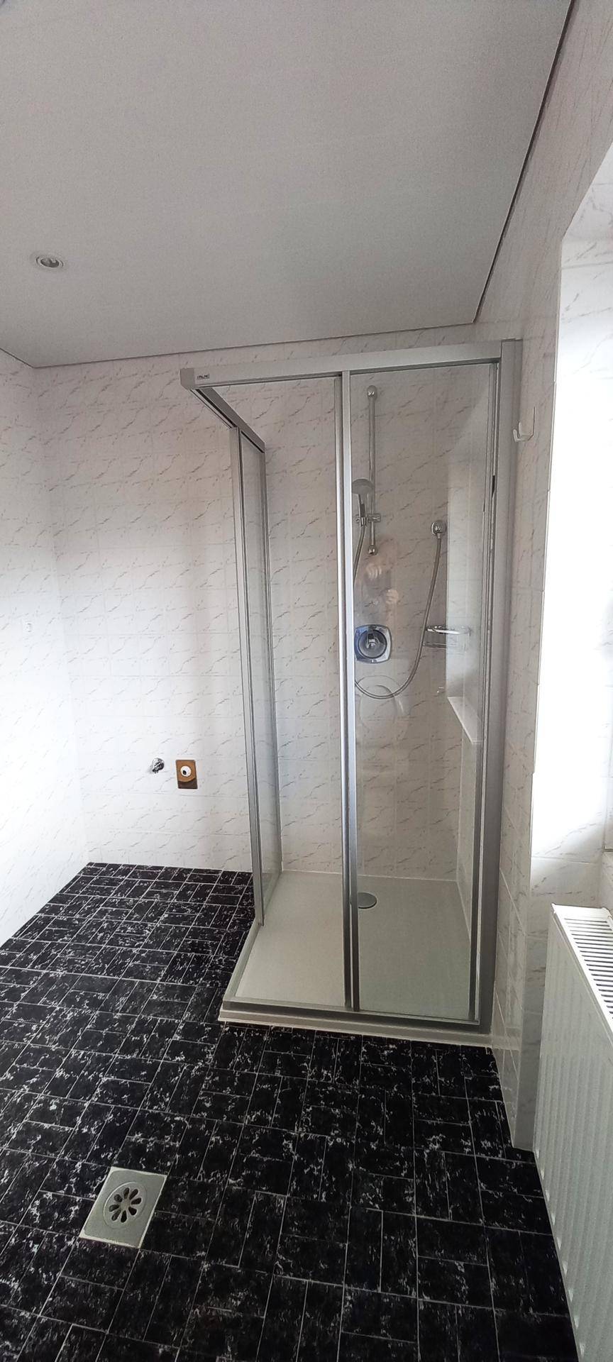 Funktionales Badezimmer mit Duschkabine, schwarzen Bodenfliesen und einem Heizkörper.