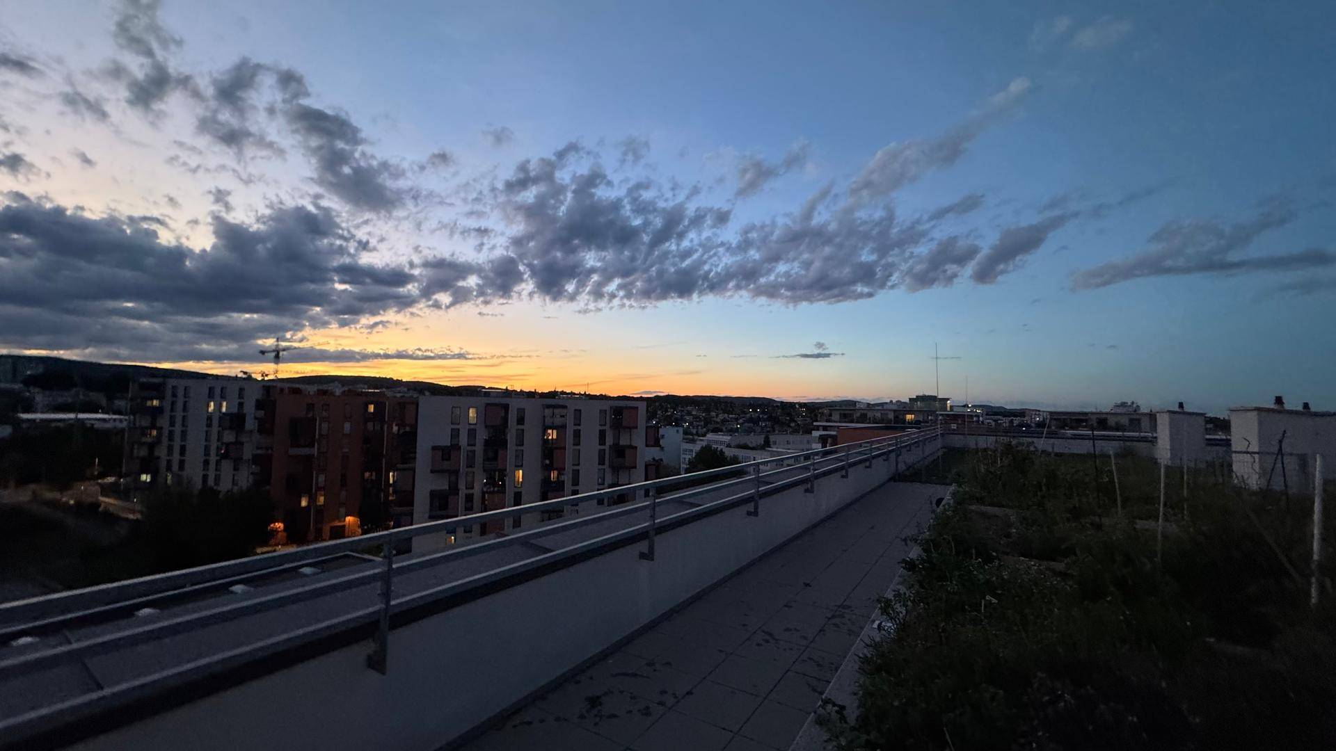 Dachgarten bei Sonnenuntergang mit Blick auf die umliegenden Gebäude und den Himmel.