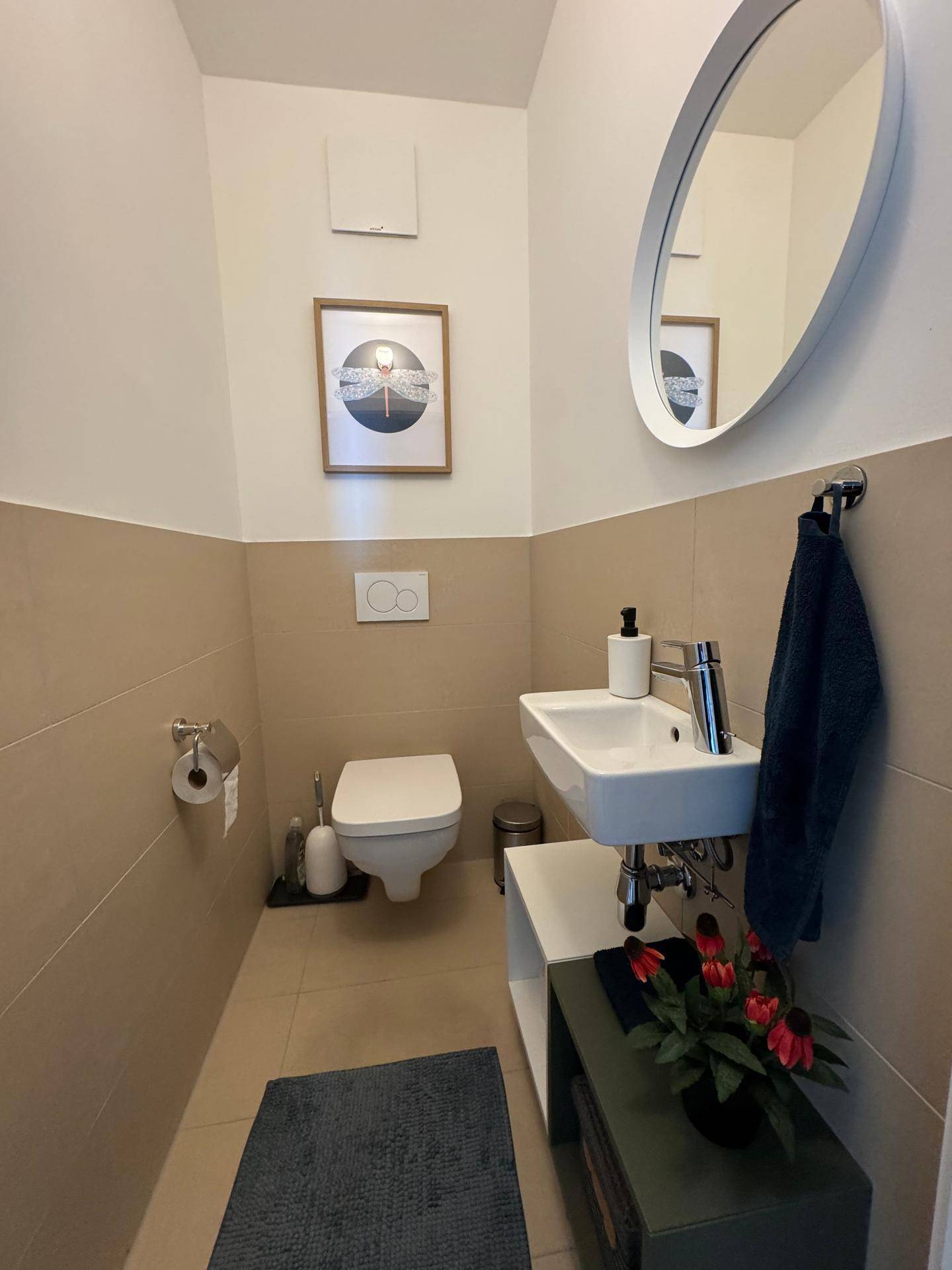 Modernes Gäste-WC mit Wand-WC, kleinem Waschbecken und beigen Fliesen.