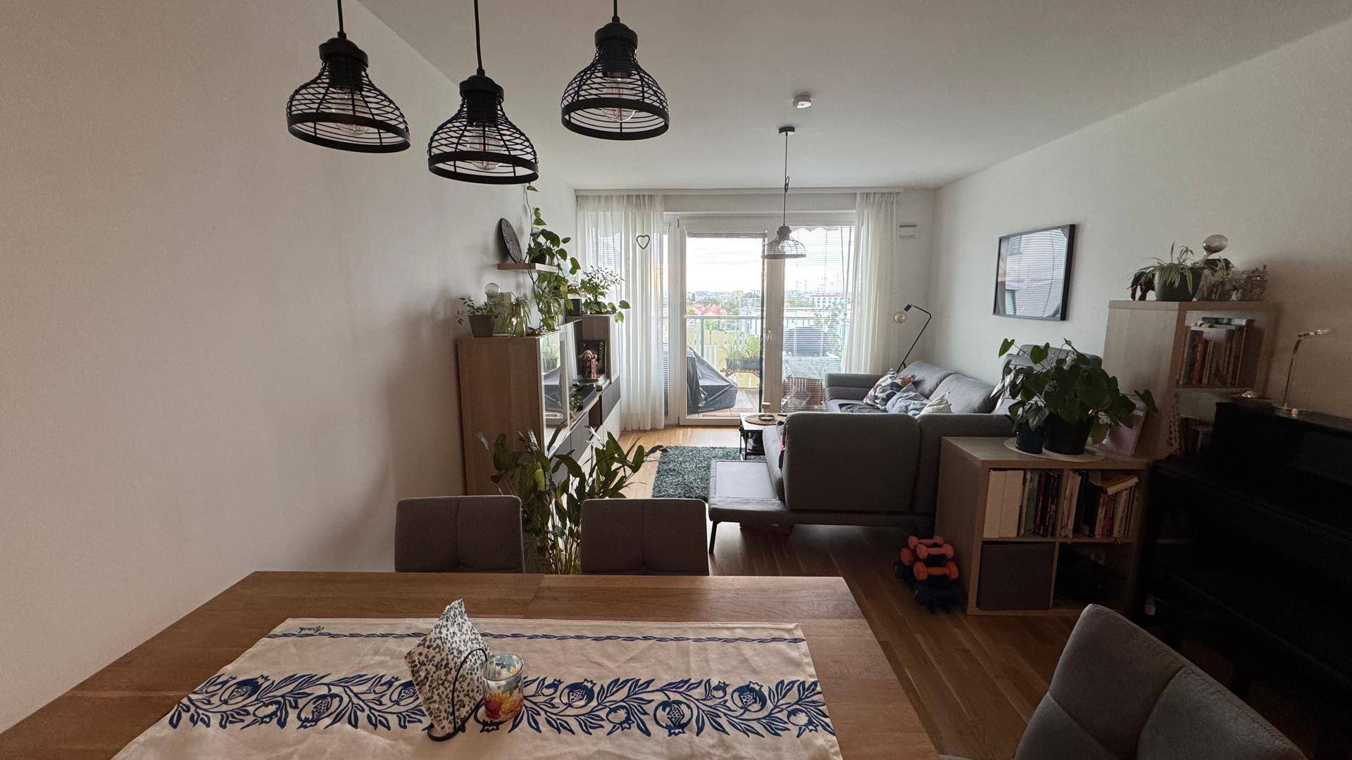 Offener Wohn-Essbereich mit Holzboden, Esstisch und Zugang zum Balkon.