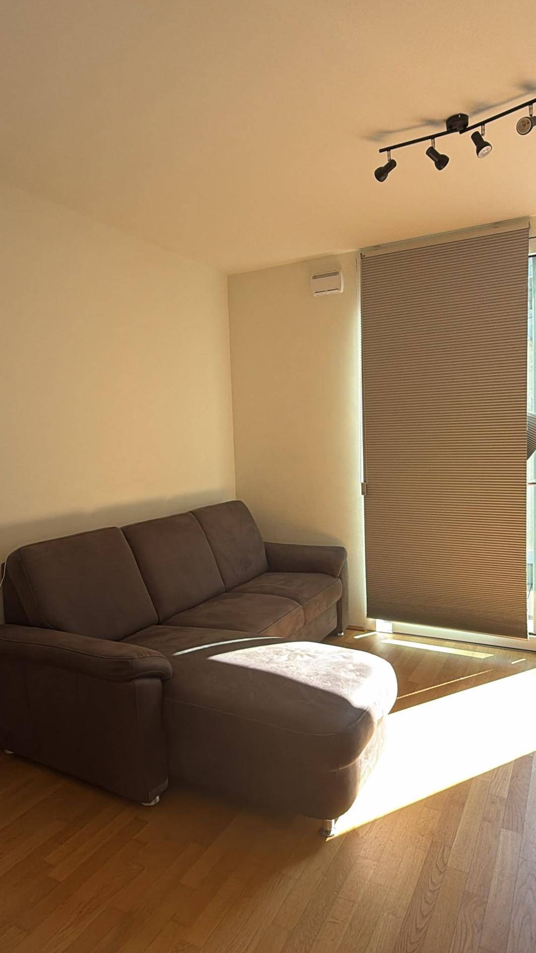 Gemütliches Wohnzimmer mit braunem Sofa, Holzfußboden und viel natürlichem Sonnenlicht durch das Fenster.