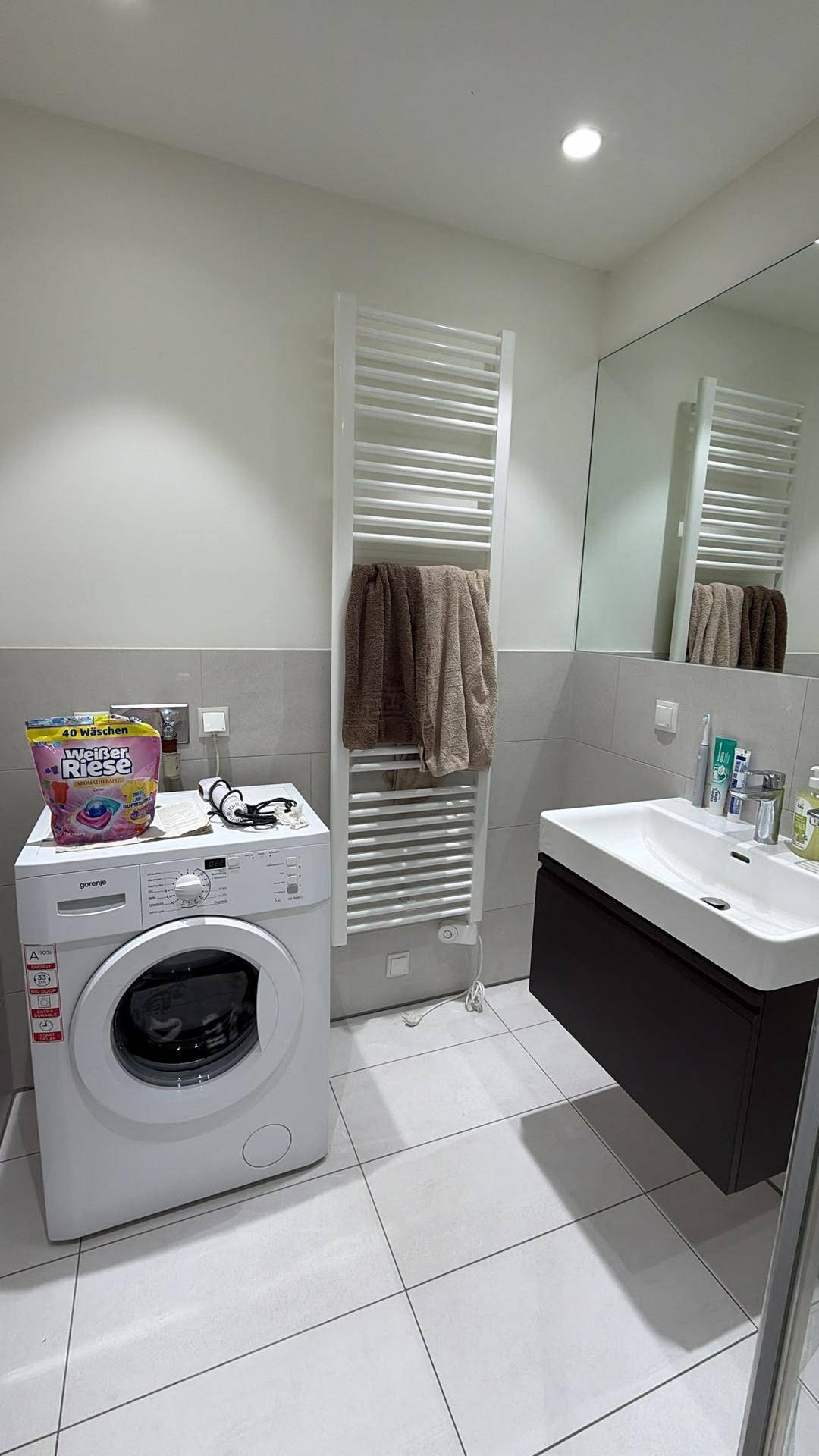 Modernes Badezimmer mit Waschmaschine, Waschbecken und beheiztem Handtuchhalter in hellem Design.