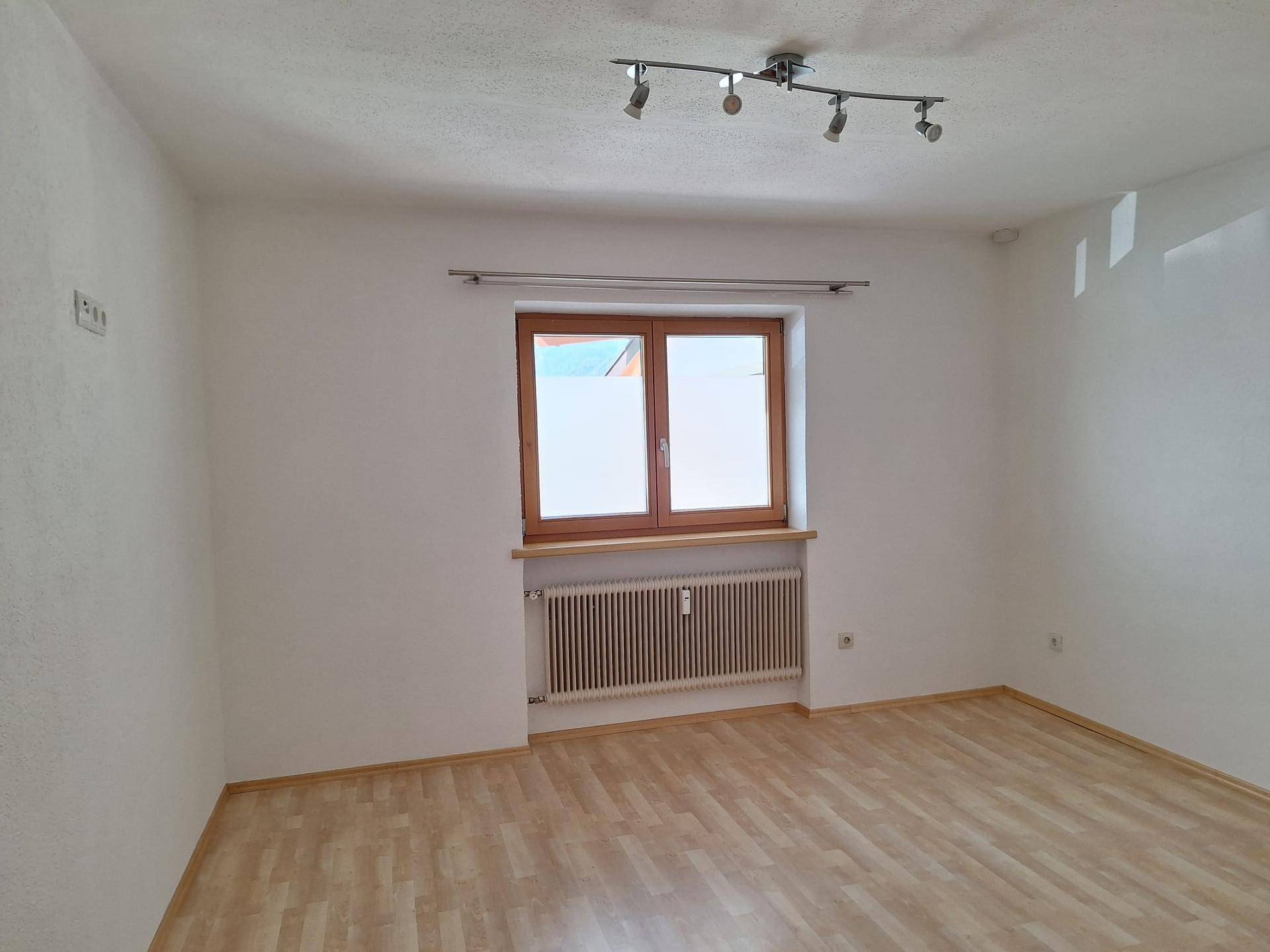 Heller, leerer Raum mit Laminatboden, Heizkörper und einem Fenster mit Holzeinfassung.