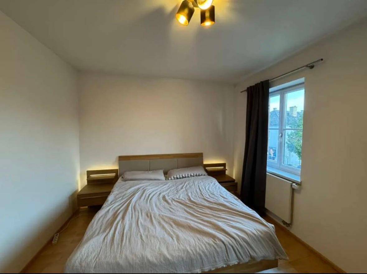 Schlafzimmer mit Doppelbett und Nachttischen, beleuchtet durch eine Deckenlampe und Fenster.