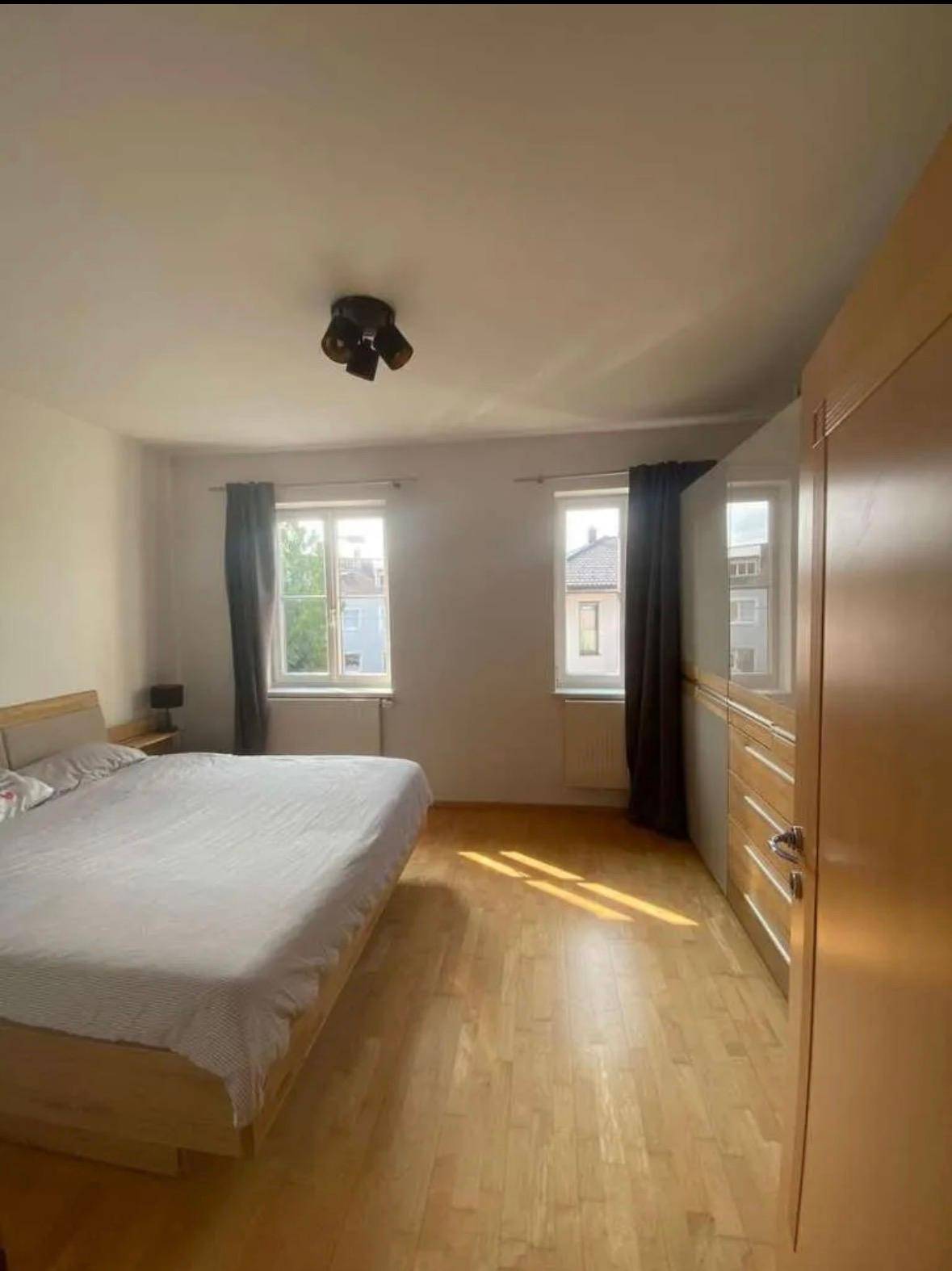 Schlafzimmer mit Doppelbett, Holzfußboden und zwei Fenstern, bietet eine ruhige Atmosphäre.