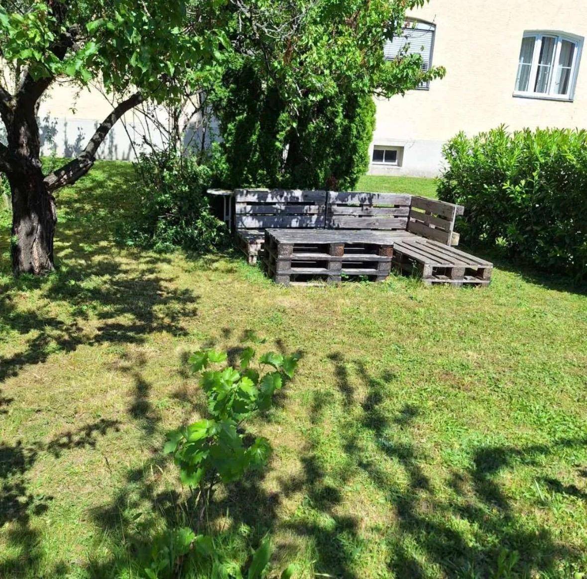 Grüner Gartenbereich mit selbstgebauten Palettenmöbeln unter einem Baum, ideal zum Entspannen.