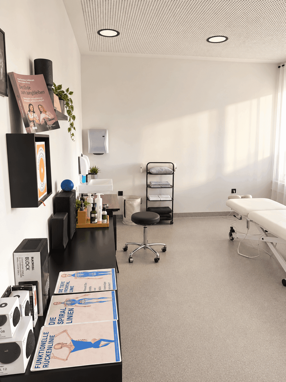 Modernes Behandlungszimmer mit weißer Liege, Regalen und einem Waschbeckenbereich.