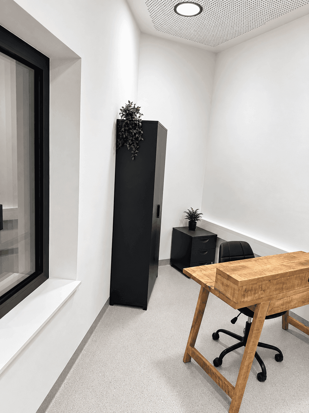 Modernes Büro mit Holztisch, schwarzem Schrank und Fenster für natürliche Belichtung.