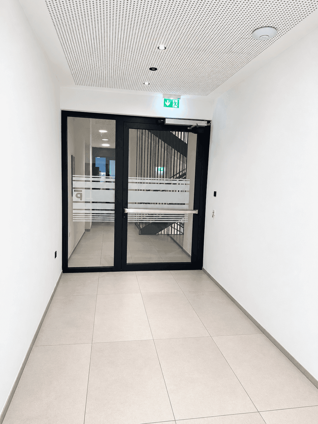 Heller Flur mit Glasdoppeltür, die zu einem Treppenhaus und weiteren Bereichen führt.