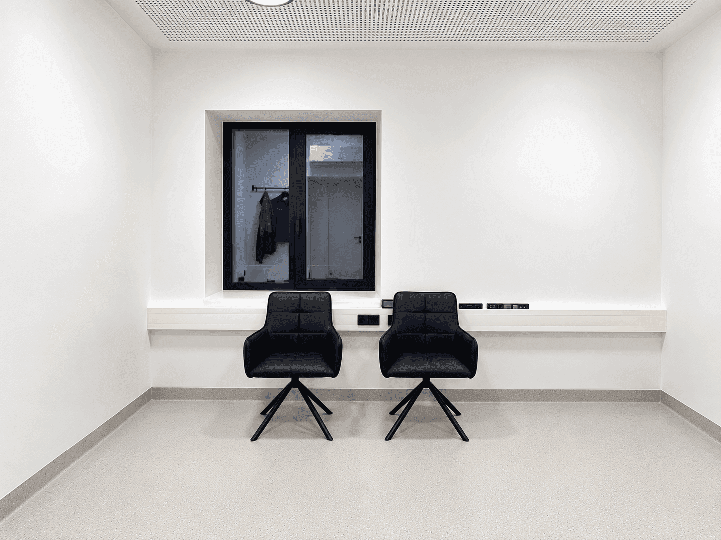 Minimalistischer Wartebereich mit zwei schwarzen Stühlen und einem Fenster mit Blick nach draußen.
