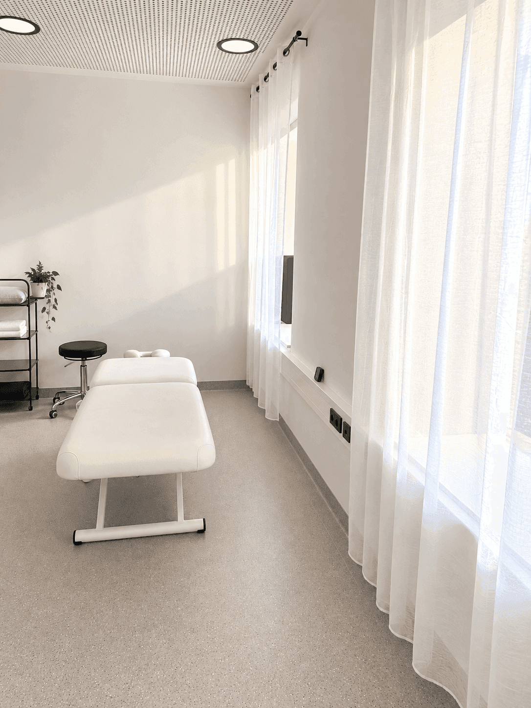 Detailansicht eines hellen Behandlungszimmers mit transparenten Vorhängen und Vinylboden.