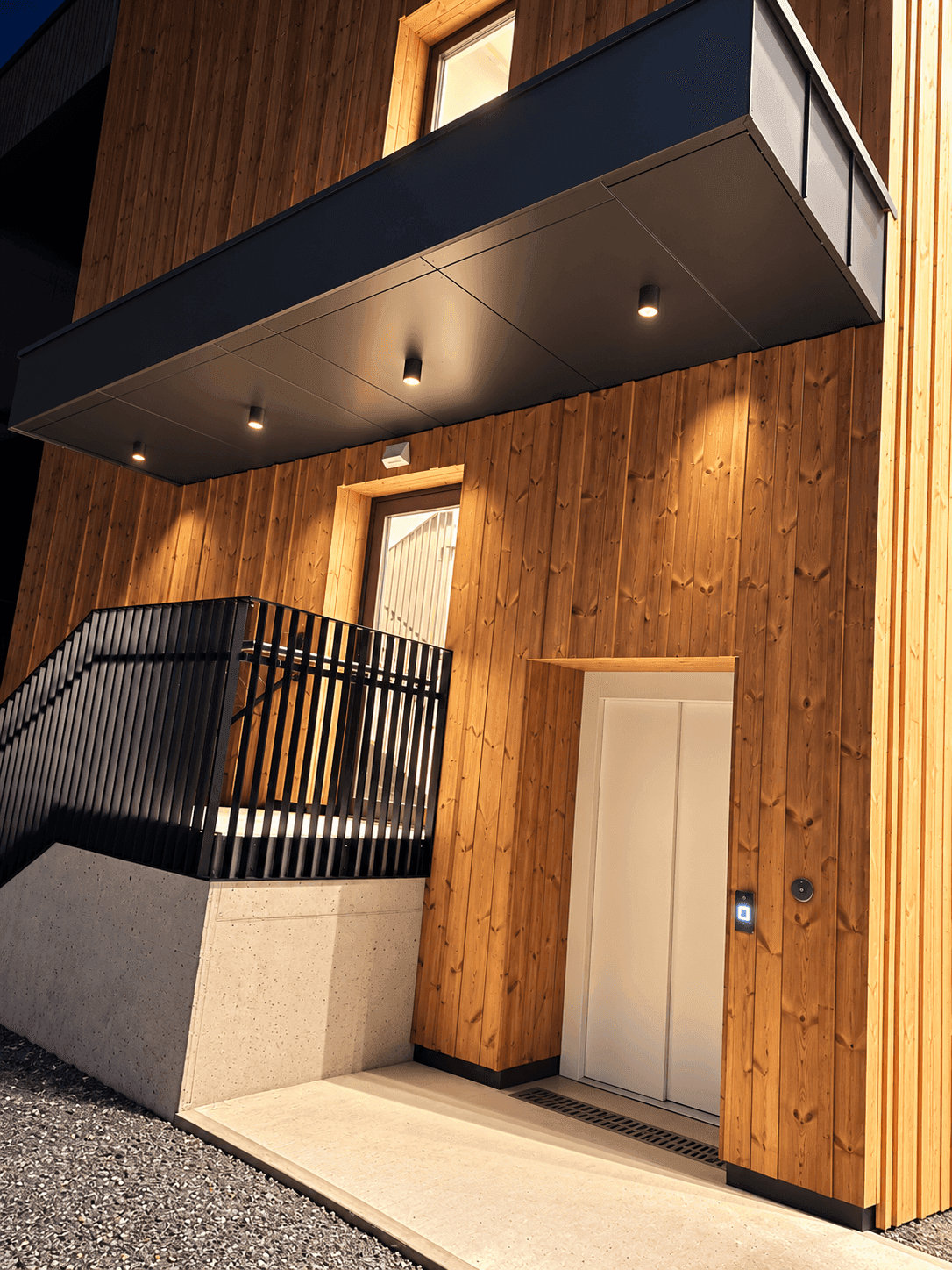 Moderne Gebäudefassade aus Holz mit einem Eingangsbereich und einem Aufzug.