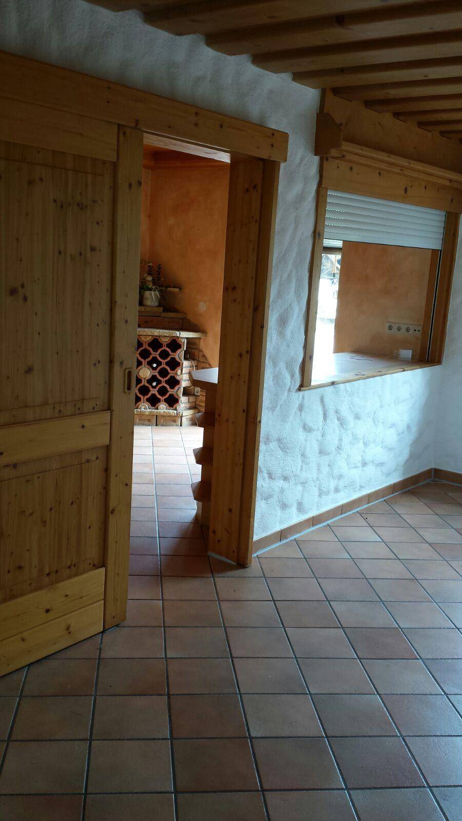 Flur mit Holztüren und Terrakottafliesen, Blick auf einen angrenzenden Raum mit Weinregal.