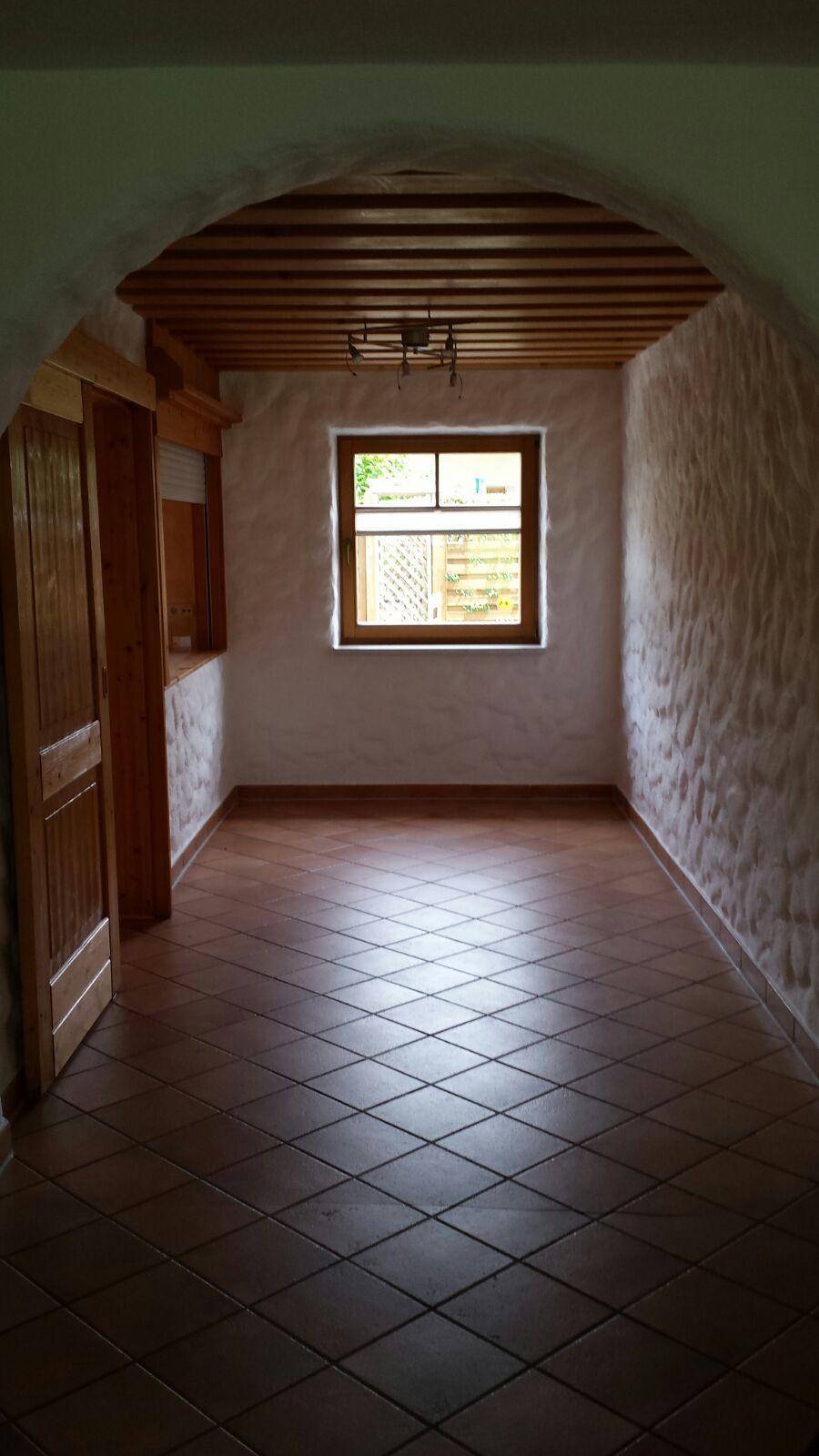 Leerer Raum mit Terrakottafliesen, Holzbalkendecke und einem Fenster.