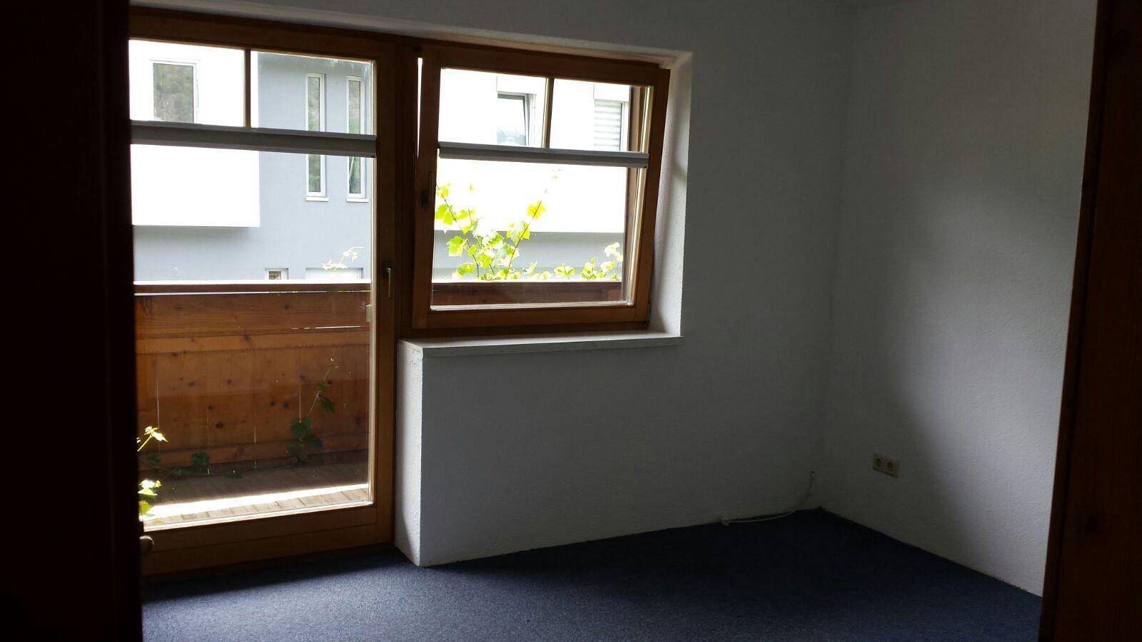 Leeres Schlafzimmer mit Teppichboden und Zugang zu einem kleinen Balkon.
