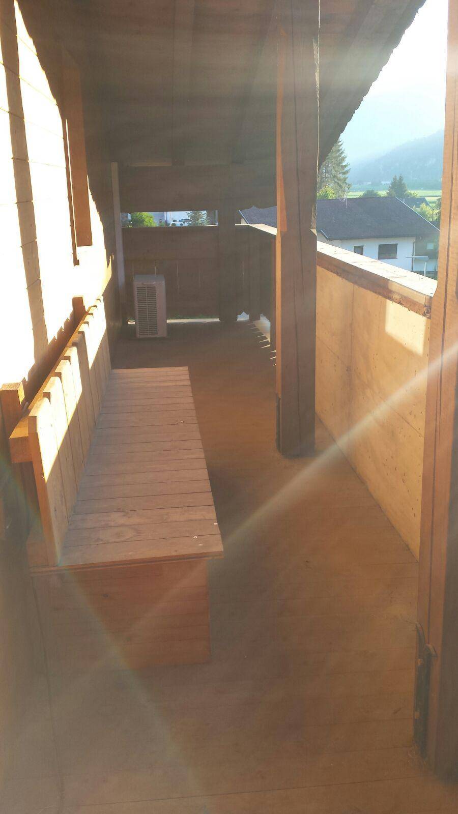 Überdachter Holzbalkon mit Sitzbank und weitem Blick ins Grüne.