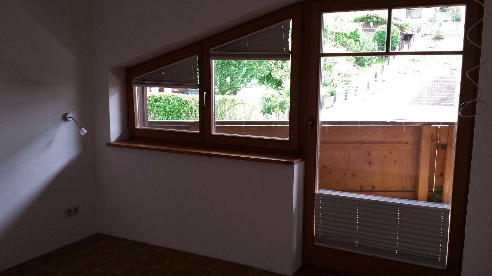 Schlafzimmer mit Holzboden, schrägen Fenstern und Balkonzugang.