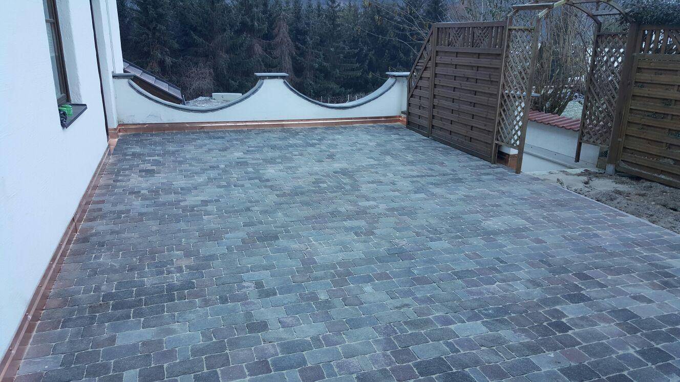 Große gepflasterte Terrasse mit dekorativer Mauer und Holzzaun.
