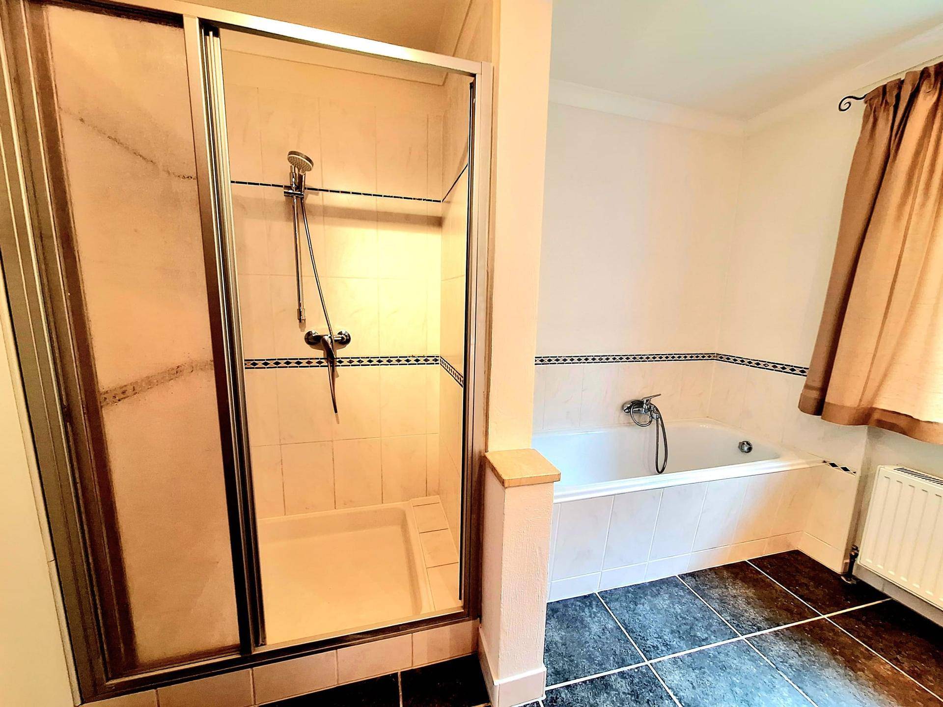 Badezimmer mit Badewanne und separater Duschkabine, gefliestem Boden und Wänden.