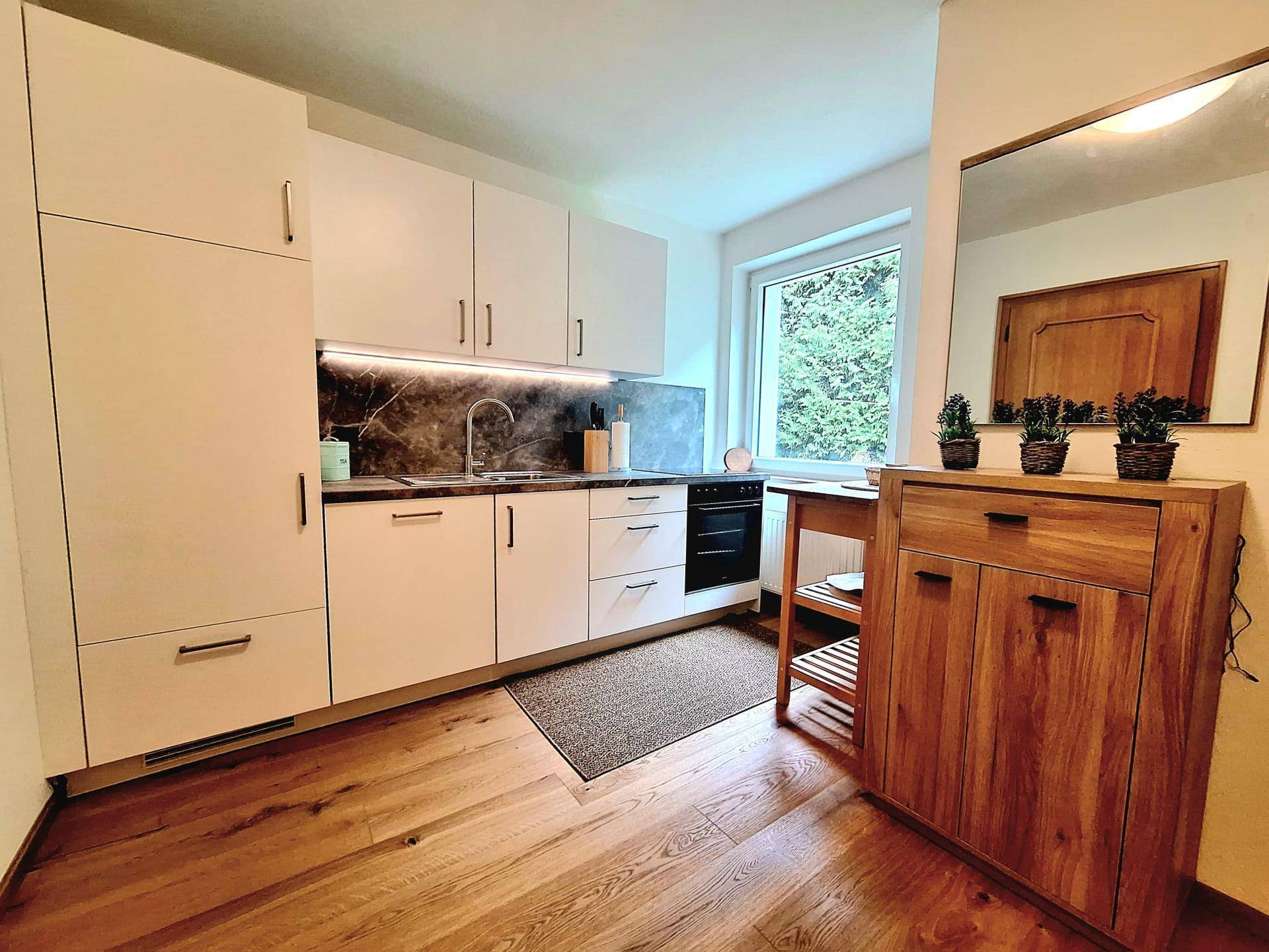 Moderne Küche mit weißen Schränken, dunkler Arbeitsplatte und Fenster mit Blick ins Grüne.