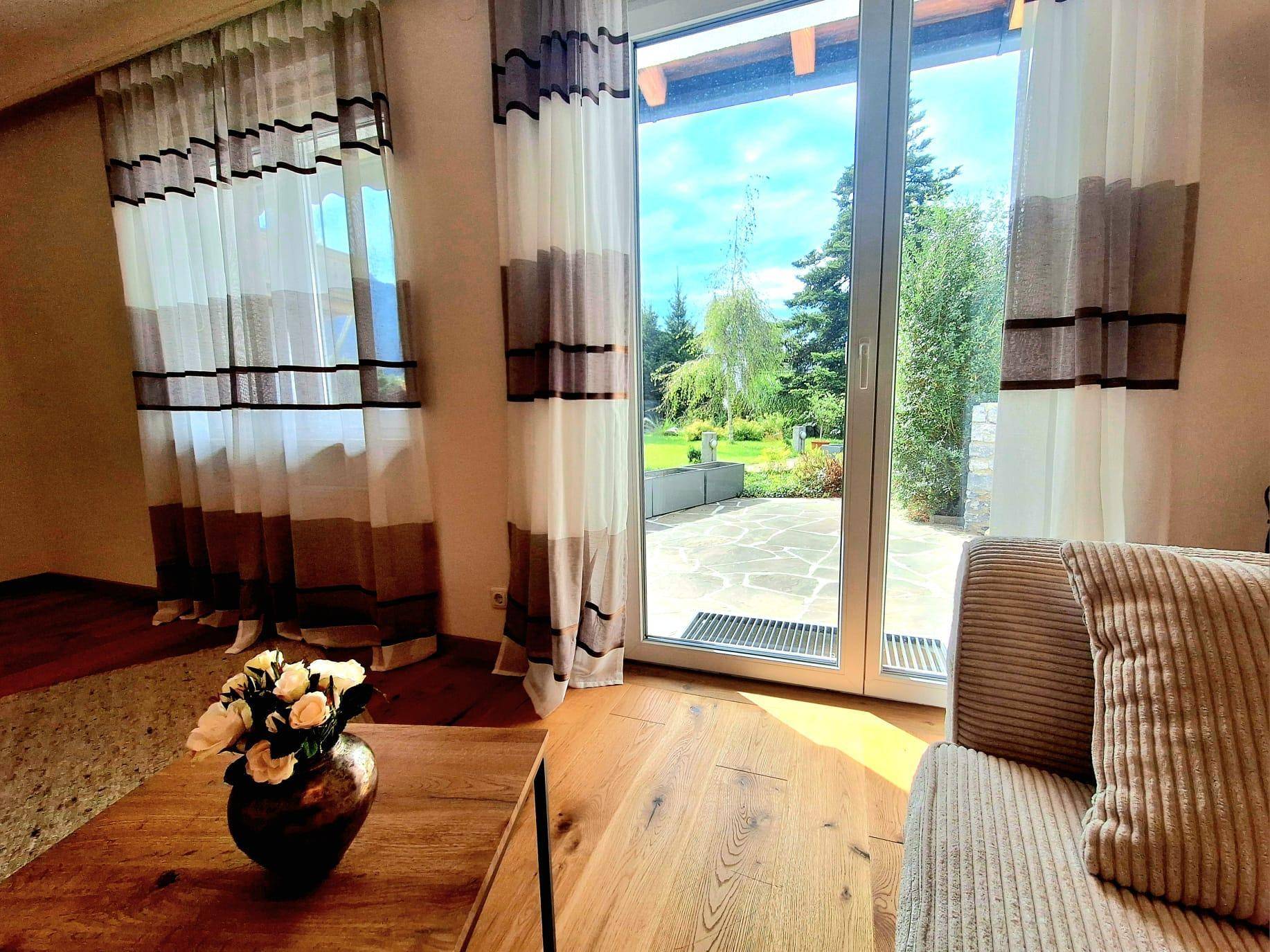 Blick aus dem Wohnzimmer durch große Fenster auf die Terrasse und den gepflegten Gartenbereich.