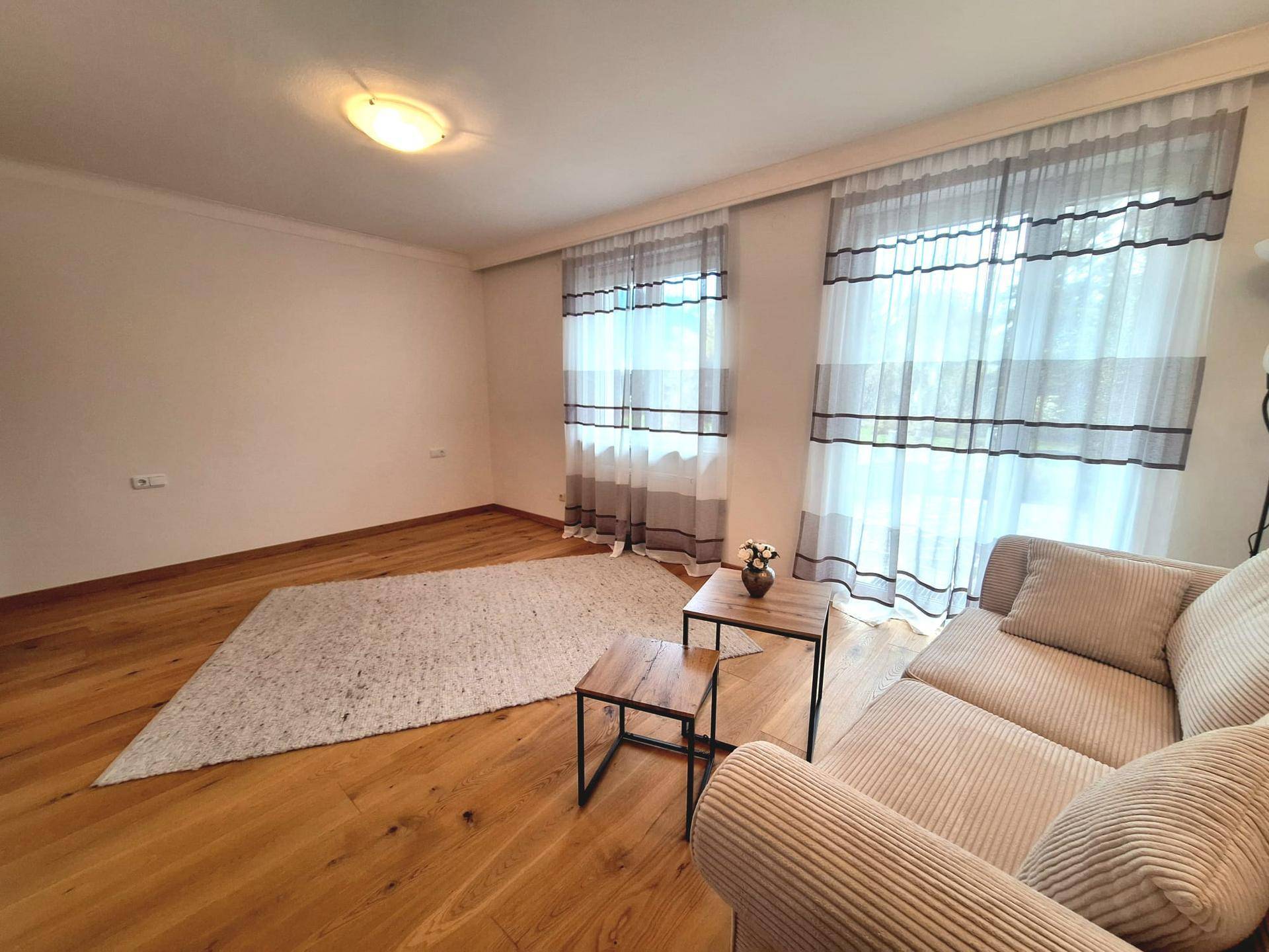 Geräumiges Wohnzimmer mit hellem Holzboden, großem Teppich und bequemer Couch.