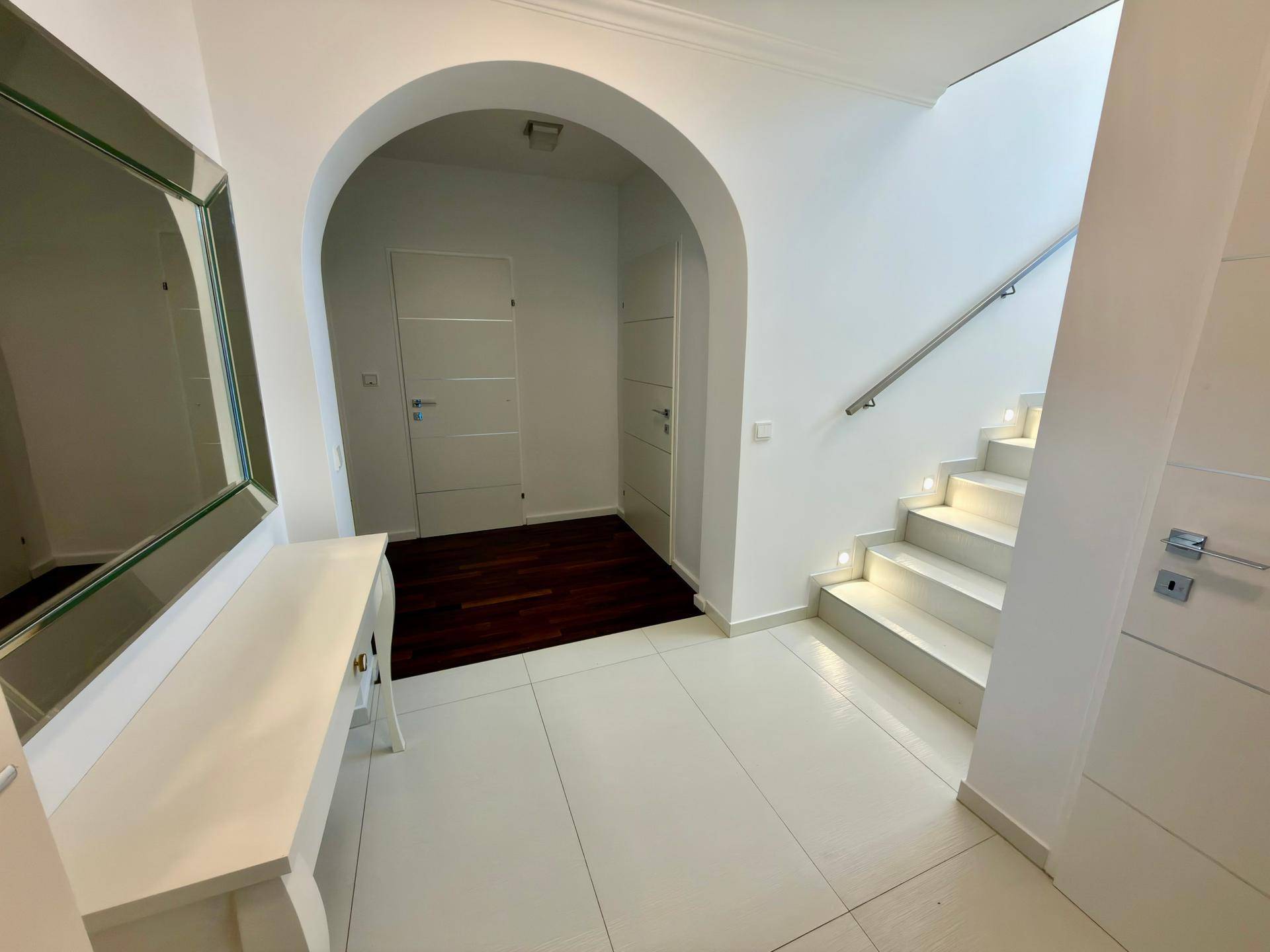 Eleganter Eingangsbereich mit weißem Fliesenboden, geschwungenem Bogen und beleuchteter Treppe.