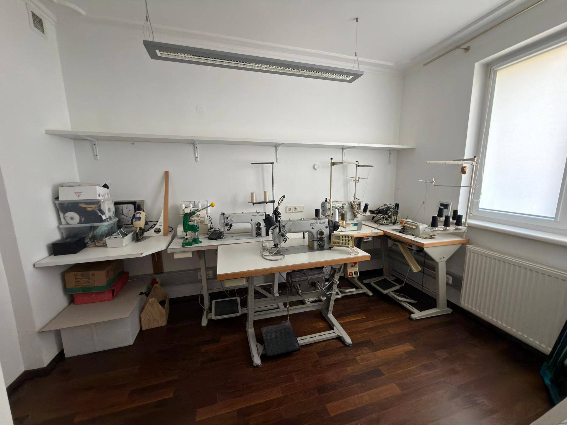 Funktionaler Arbeitsraum mit mehreren Nähmaschinen, Regalen und Holzboden.