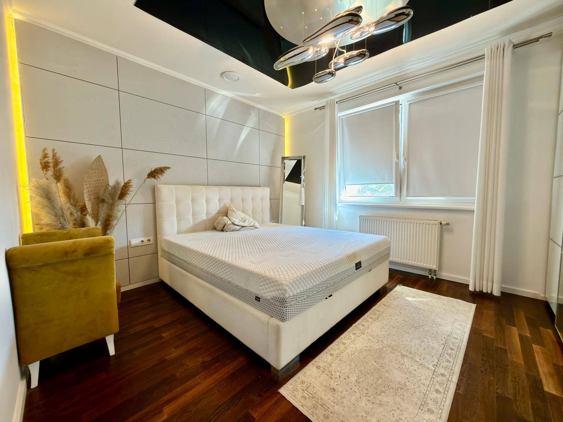 Elegantes Schlafzimmer mit großem weißen Bett, gelbem Sessel und moderner Deckenbeleuchtung.