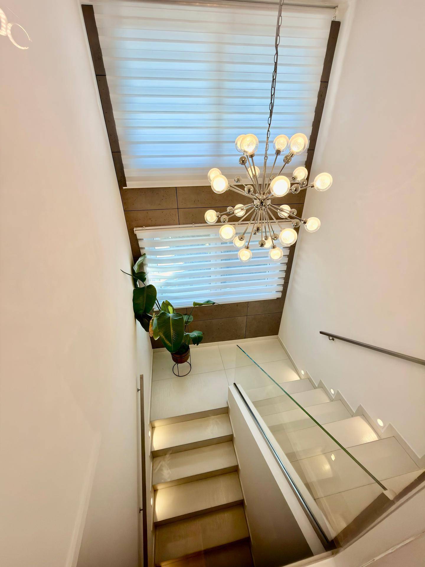 Elegantes Treppenhaus mit modernen Stufen, Glasgeländer und stilvoller Hängelampe.