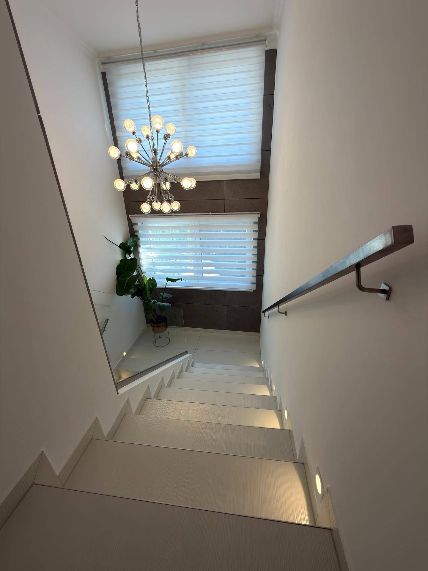 Elegantes Treppenhaus mit modernen Stufen, Glasgeländer und stilvoller Hängelampe.