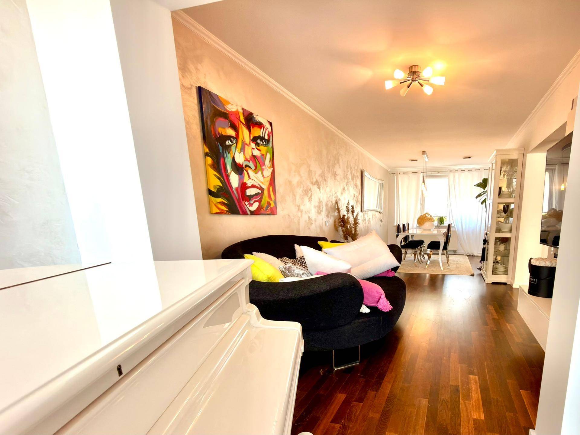 Geräumiger Wohn-Essbereich mit dunklem Sofa, farbenfroher Kunst und elegantem Holzboden.