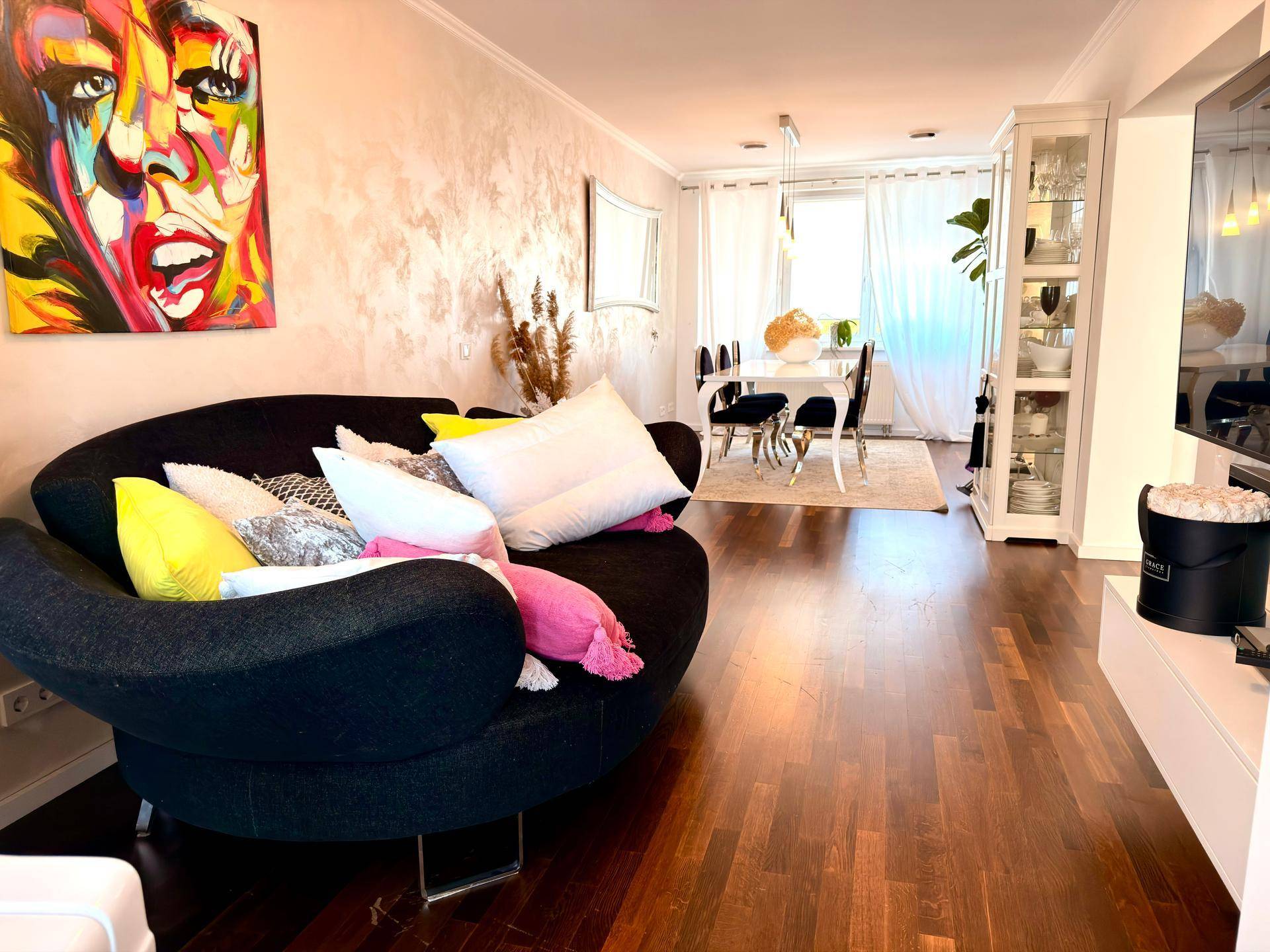 Geräumiger Wohn-Essbereich mit dunklem Sofa, farbenfroher Kunst und elegantem Holzboden.