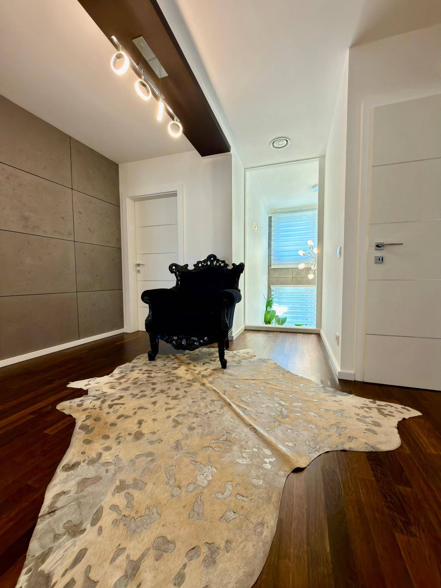 Moderner Flur mit dunklem Holzboden, dekorativem Sessel und Akzentwand in Betonoptik.