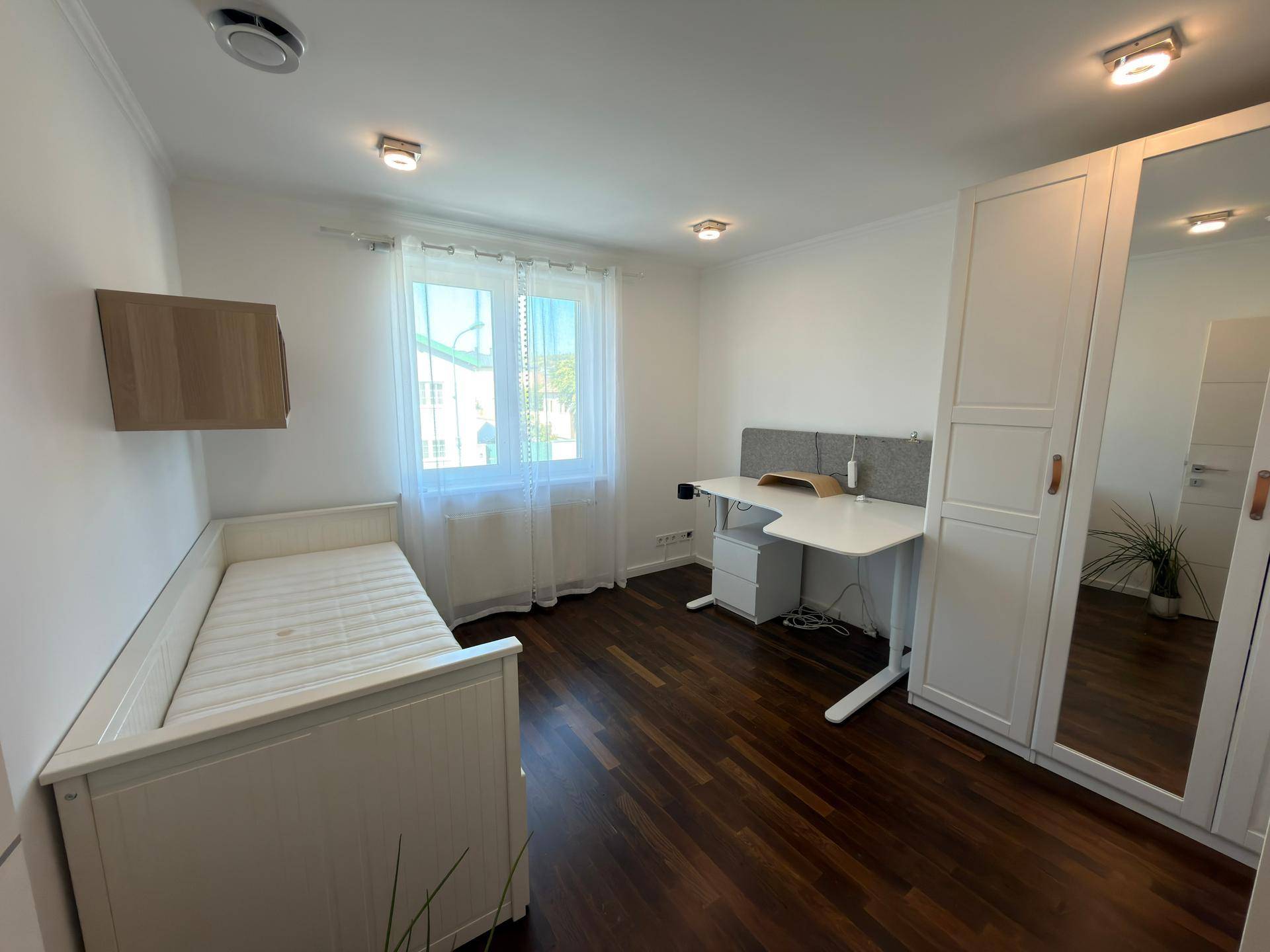 Helles Schlafzimmer mit Einzelbett, Schreibtisch und Spiegelschrank.