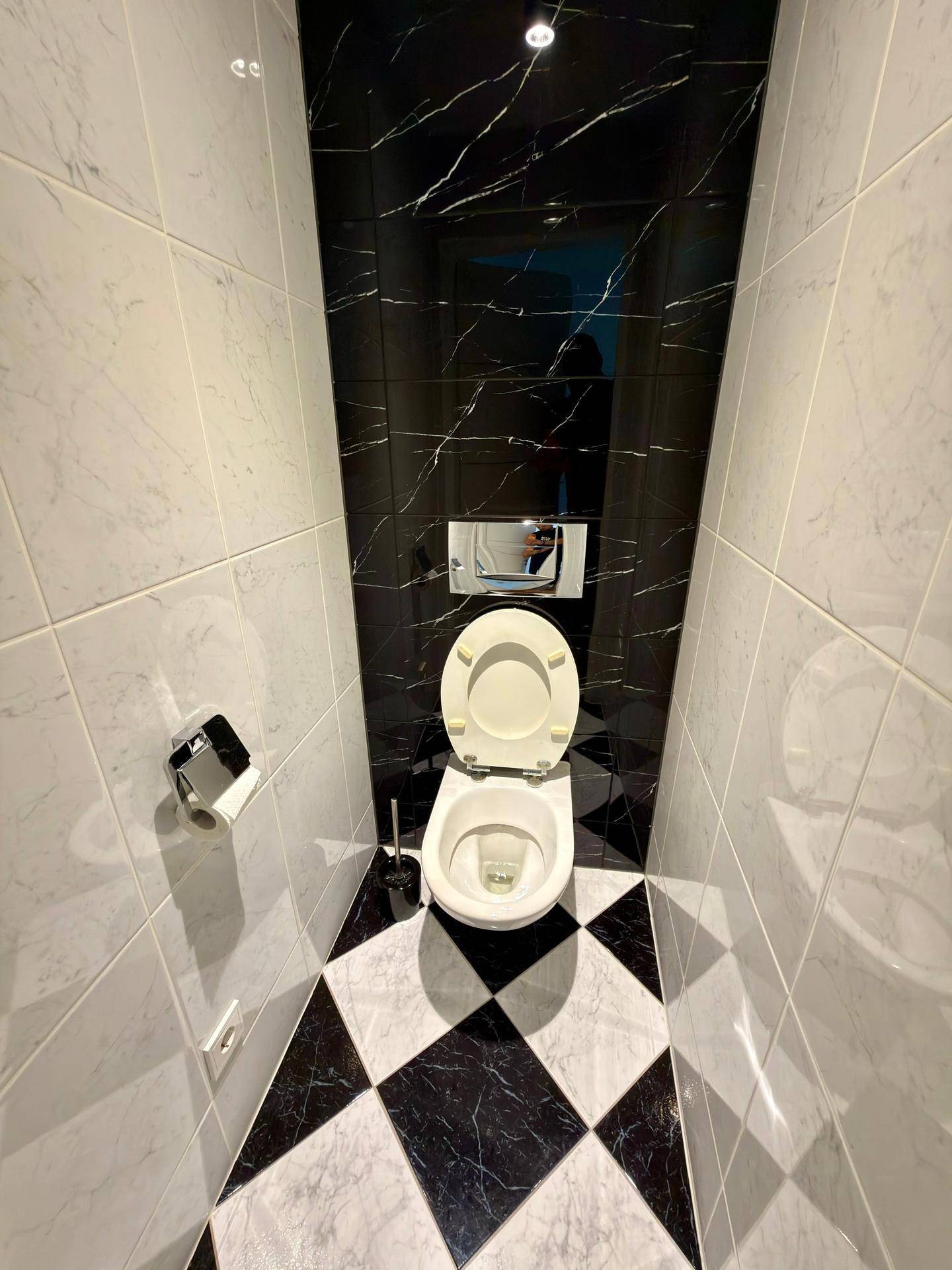 Modernes WC mit schwarz-weiß gefliestem Boden und Wänden sowie wandhängendem WC.