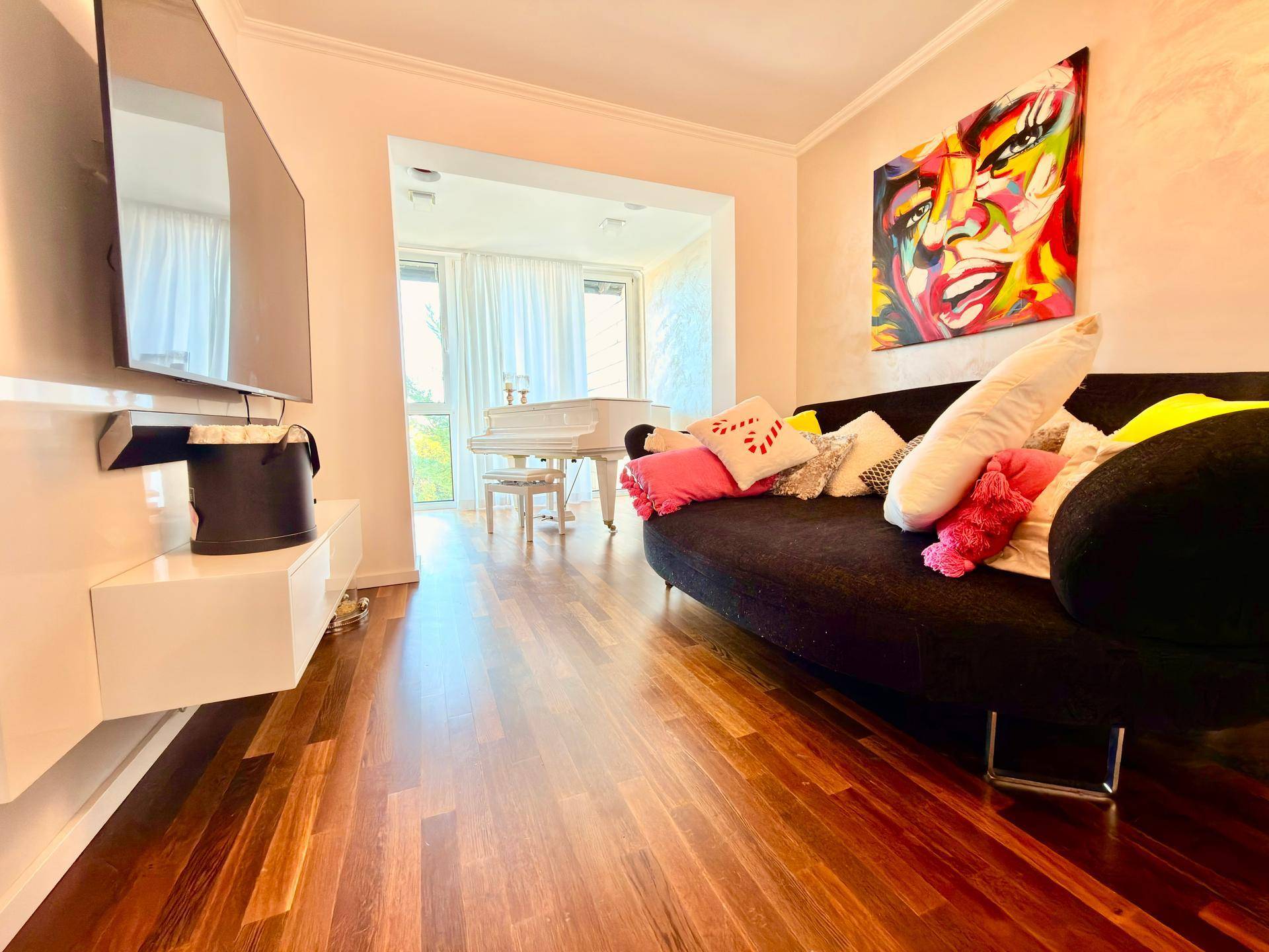 Gemütlicher Wohnbereich mit Wandfernseher, dunklem Sofa und Blick auf den Klavierbereich.