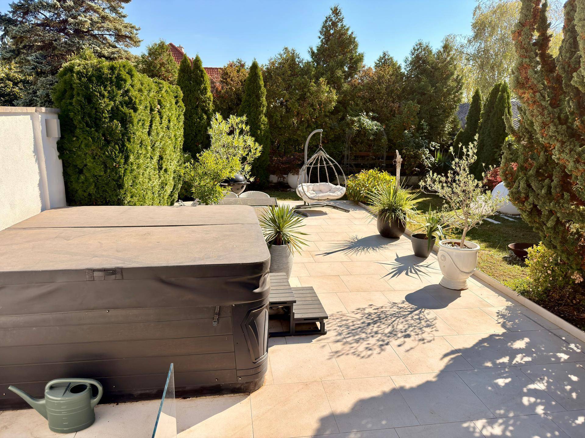 Sonniger Gartenbereich mit Whirlpool, gepflasterter Terrasse und üppiger Bepflanzung.