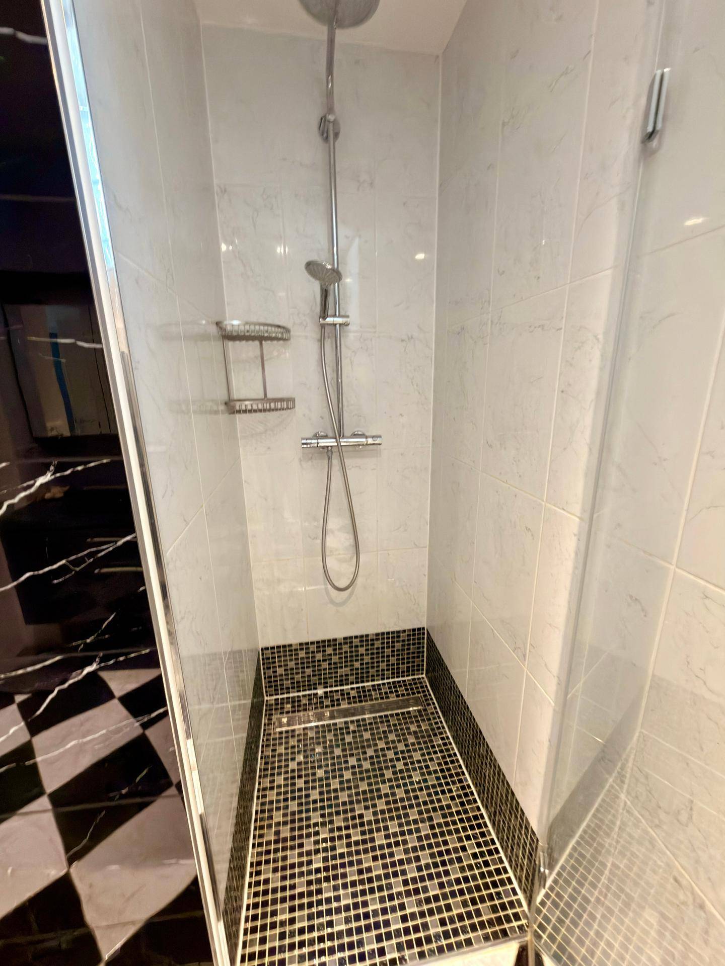 Moderne Duschkabine mit weißen Fliesen und schwarzem Mosaikboden.