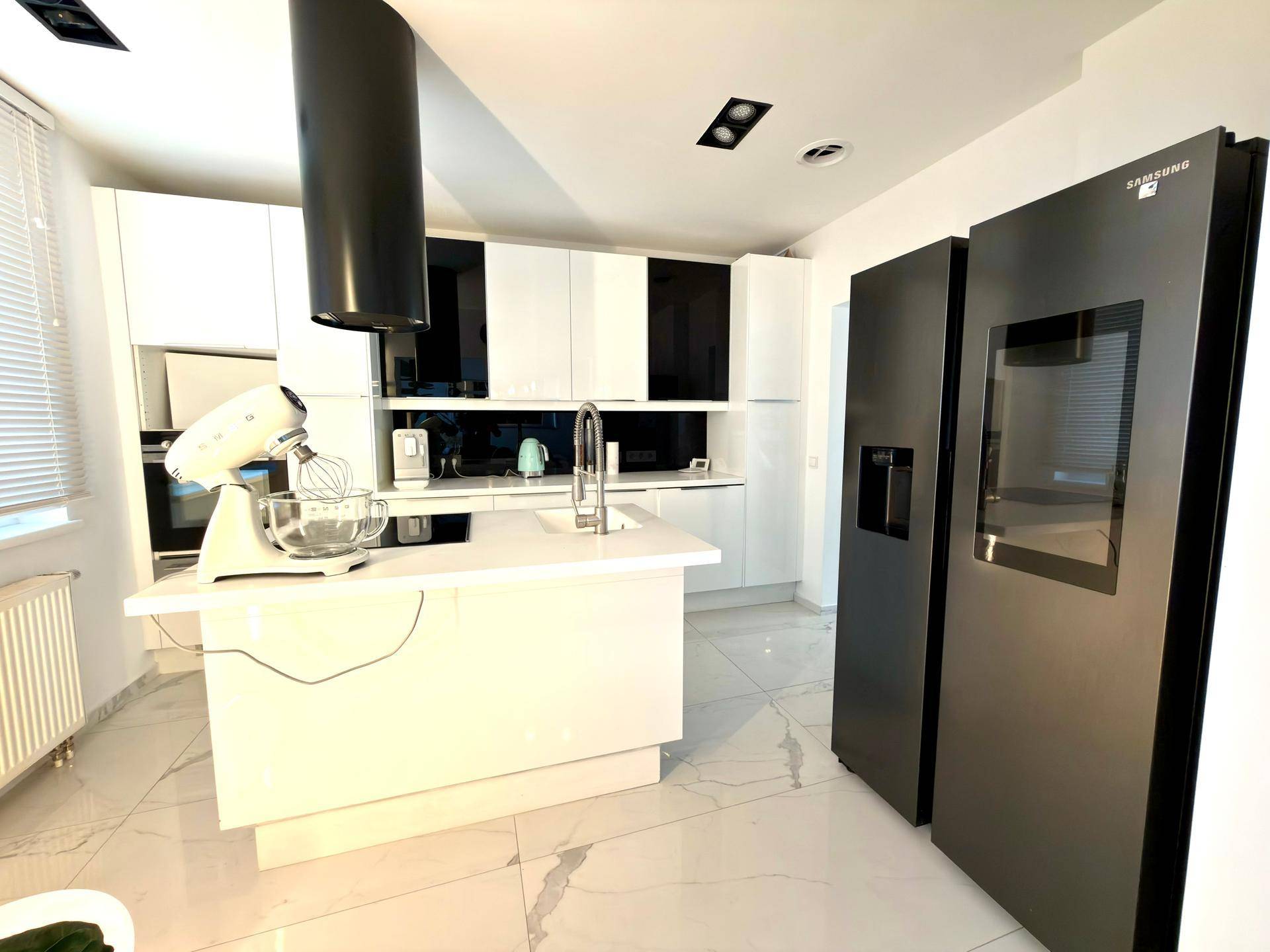Moderne Küche mit weißen Hochglanzfronten, Kochinsel und großem schwarzem Kühlschrank.