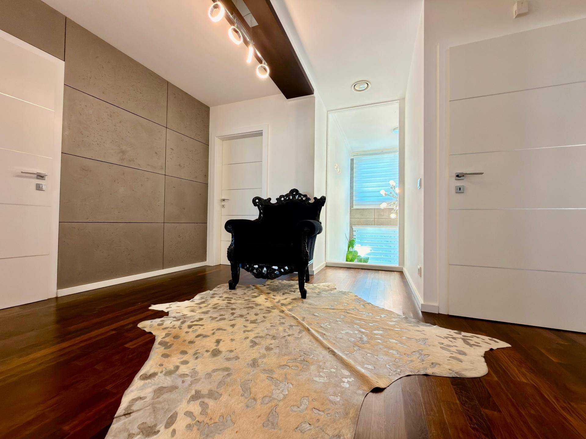 Moderner Flur mit dunklem Holzboden, dekorativem Sessel und Akzentwand in Betonoptik.
