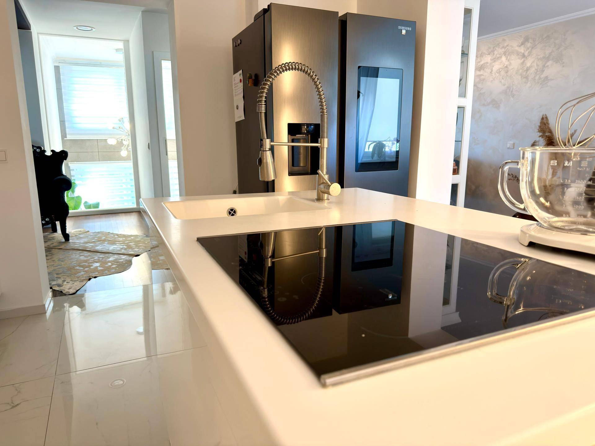 Moderne Kücheninsel mit Induktionskochfeld und Spülbecken, im Hintergrund ein großer Kühlschrank.