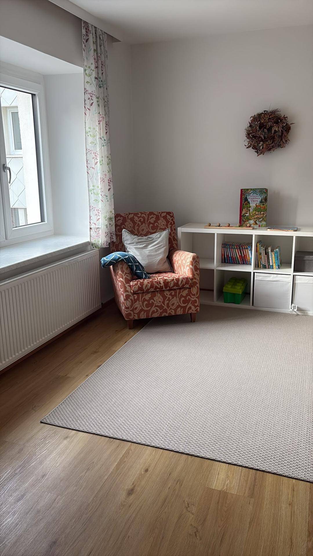 Gemütlicher Wohnbereich mit Sessel, Bücherregal und Holzboden, der viel natürliches Licht erhält.