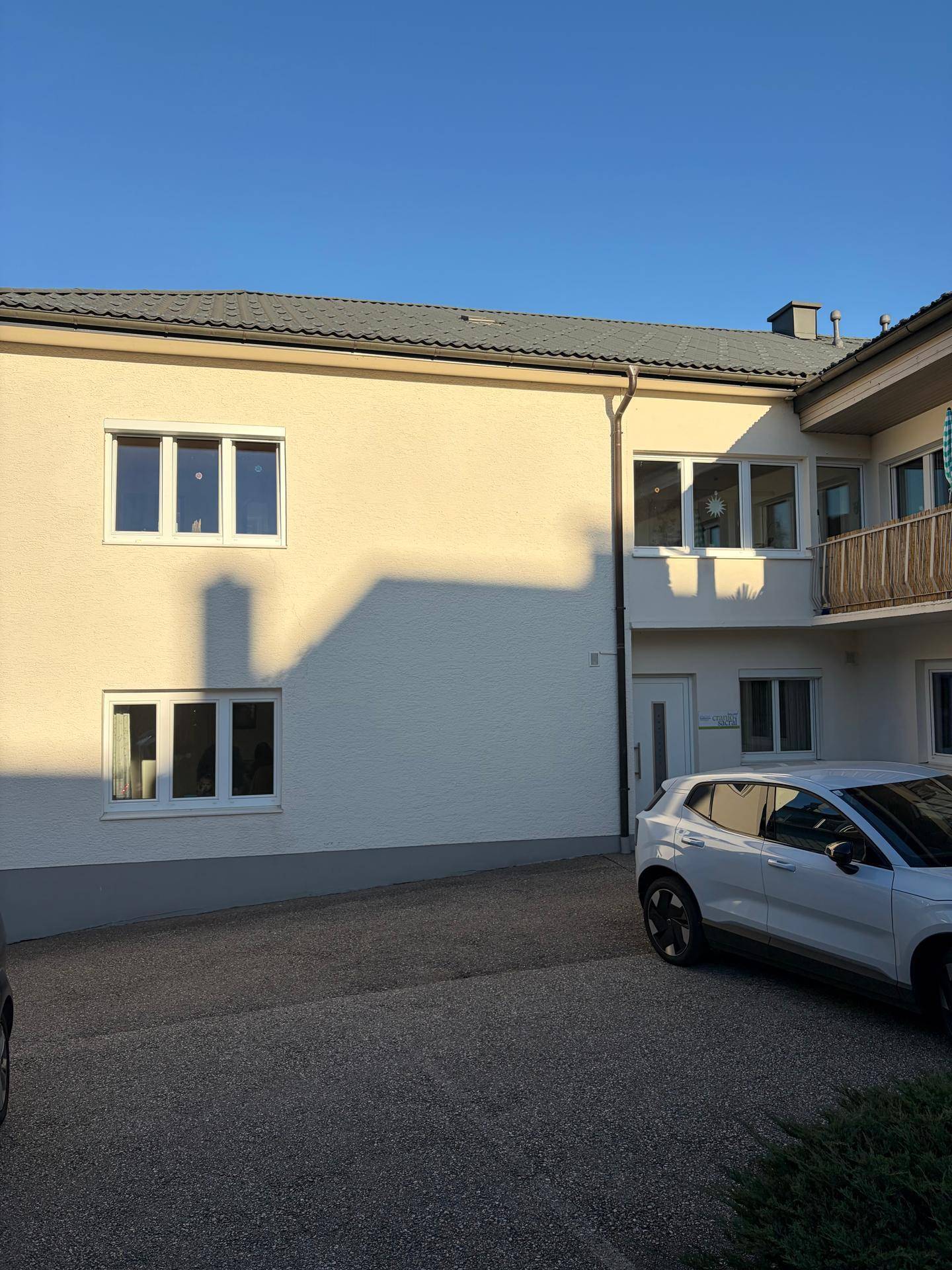 Gebäudefassade mit mehreren Fenstern und einem geparkten Auto davor unter blauem Himmel.
