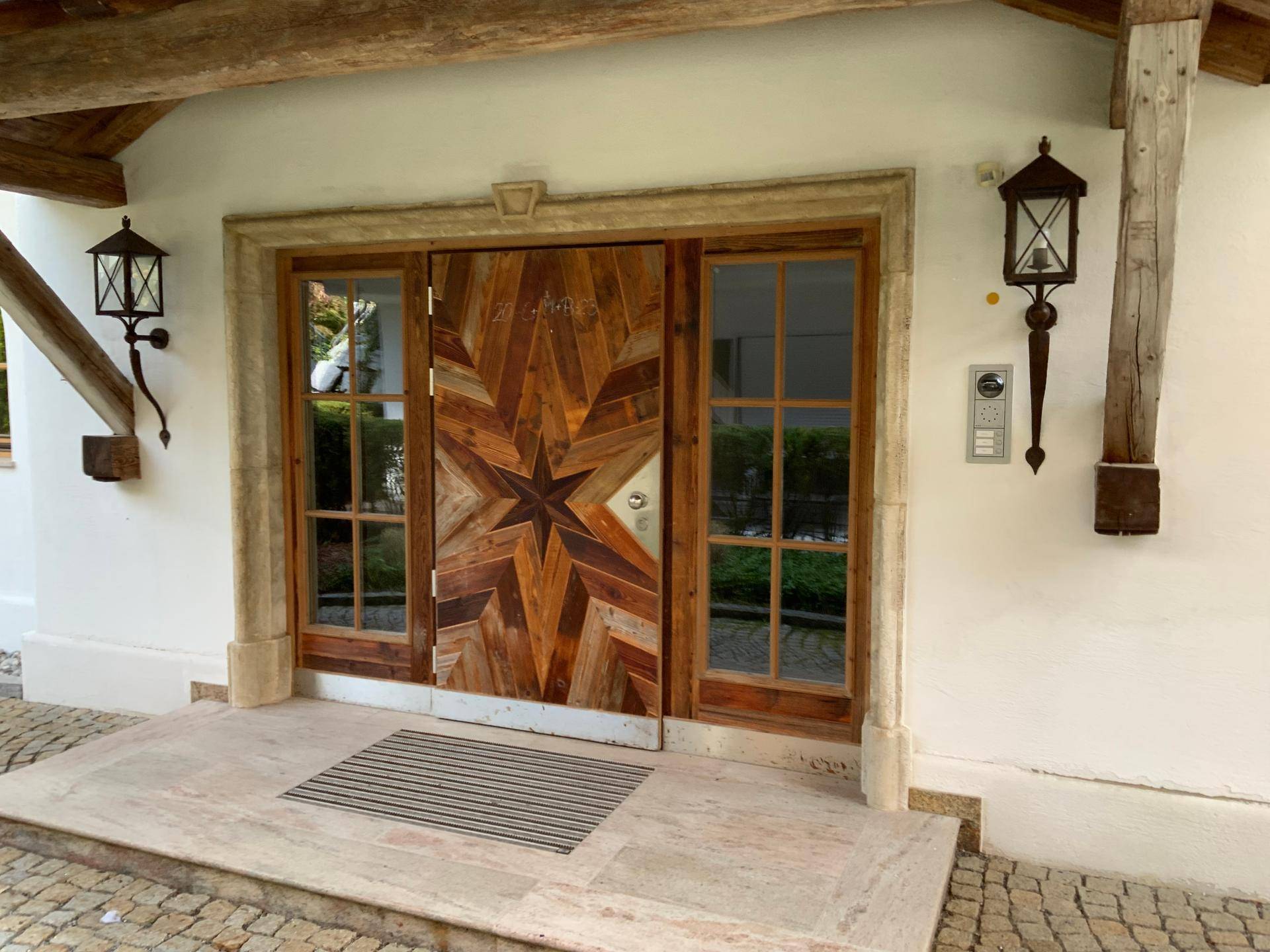 Einladender Haupteingang mit kunstvoller Holztür im Sternmuster und traditionellen Laternen.