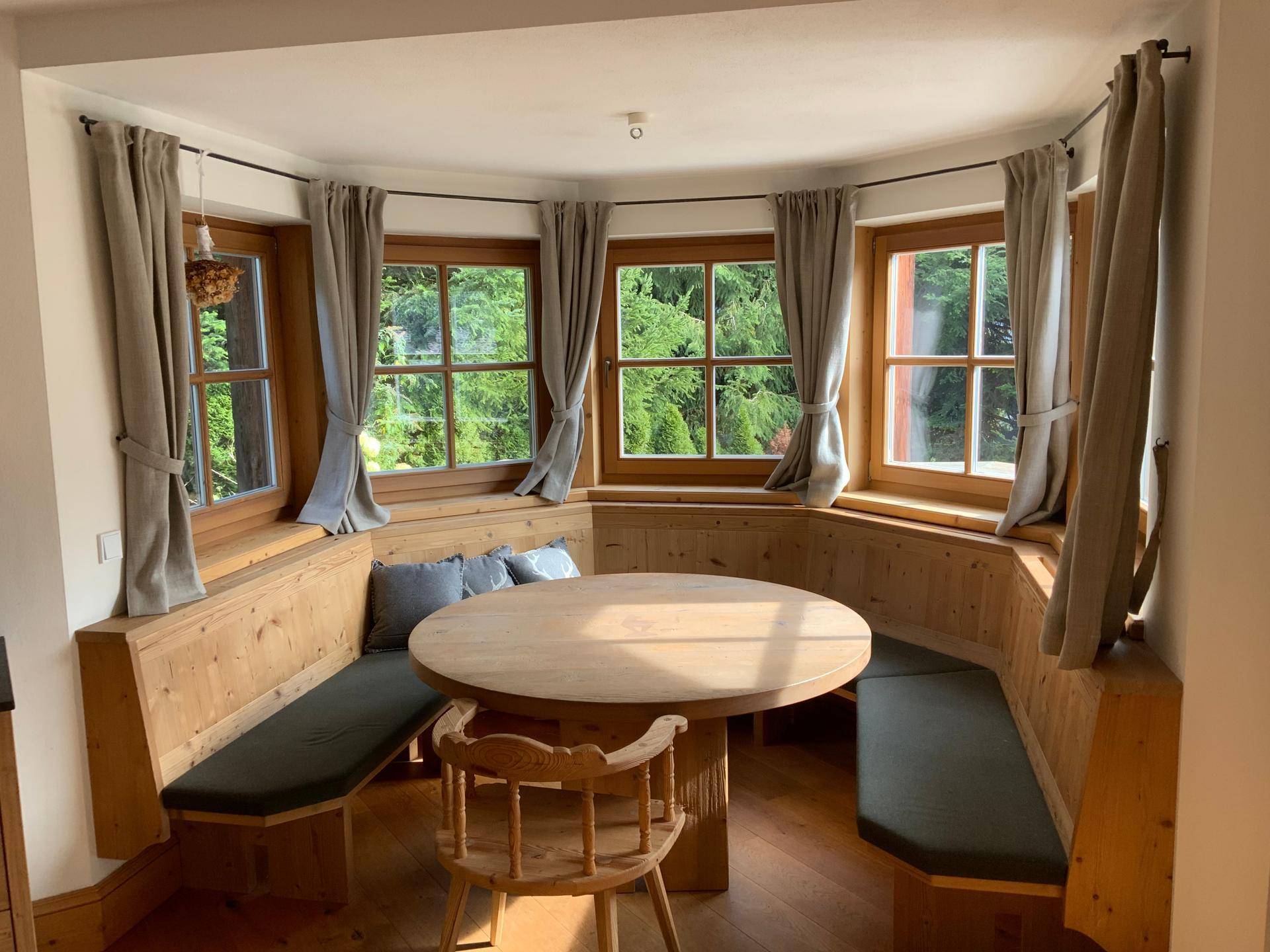 Gemütliche Essecke mit eingebauten Holzbänken, rundem Tisch und Blick ins Grüne.